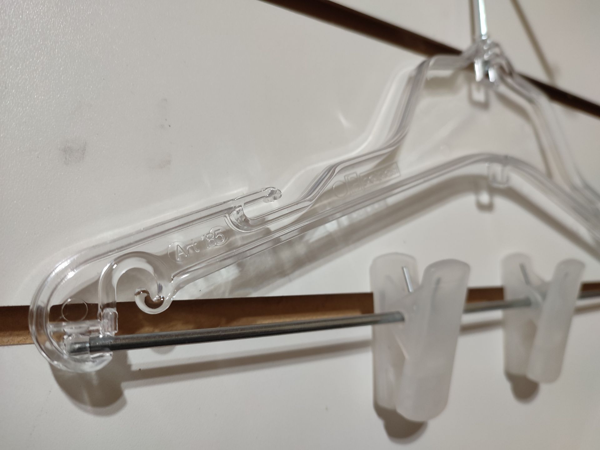 Percha de ropa de plástico transparente con pinzas sobre un fondo blanco y marrón.