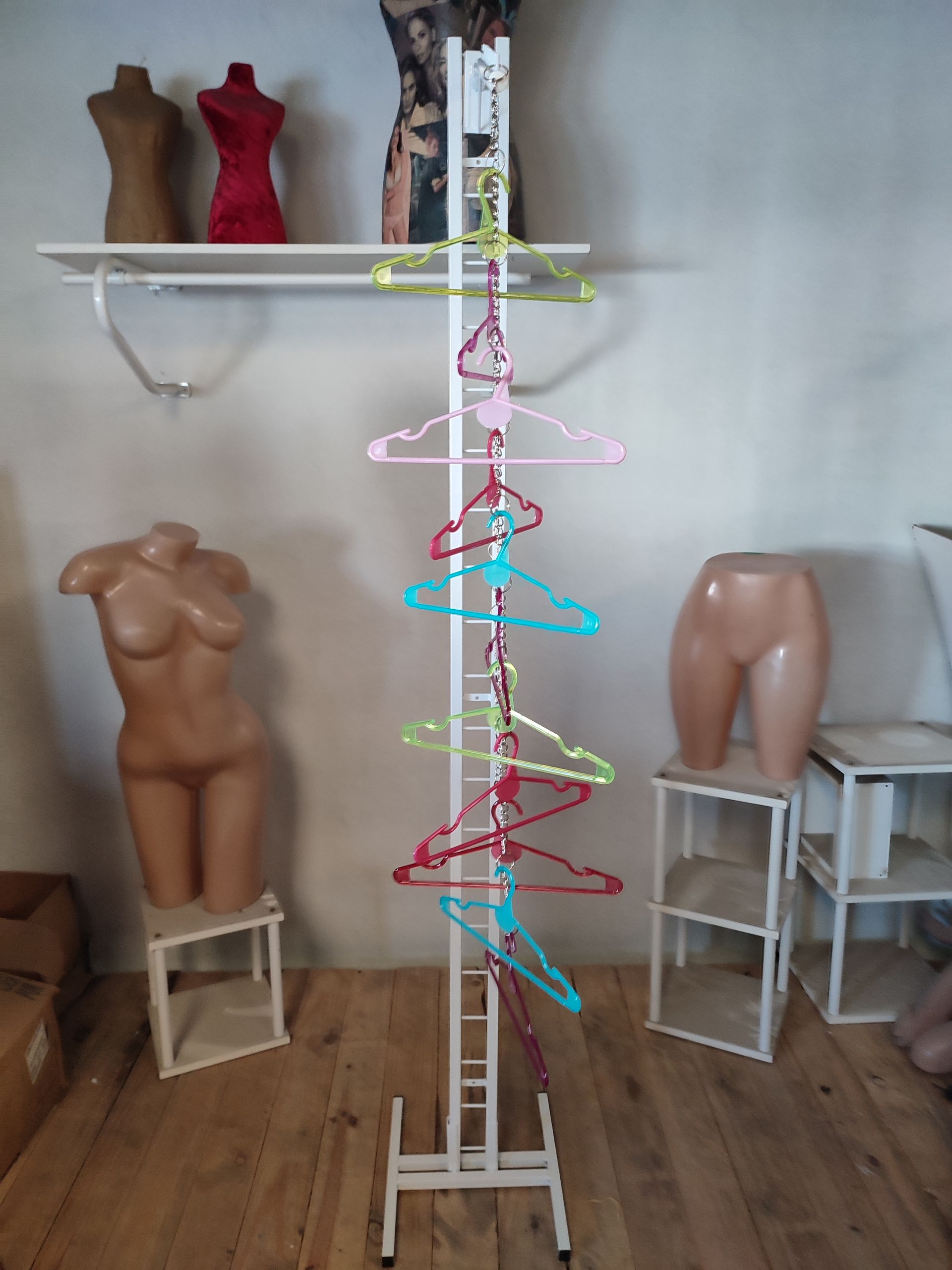 Tienda de ropa: Exhibidor con perchas de colores, maniquíes, estanterías y piso de madera.