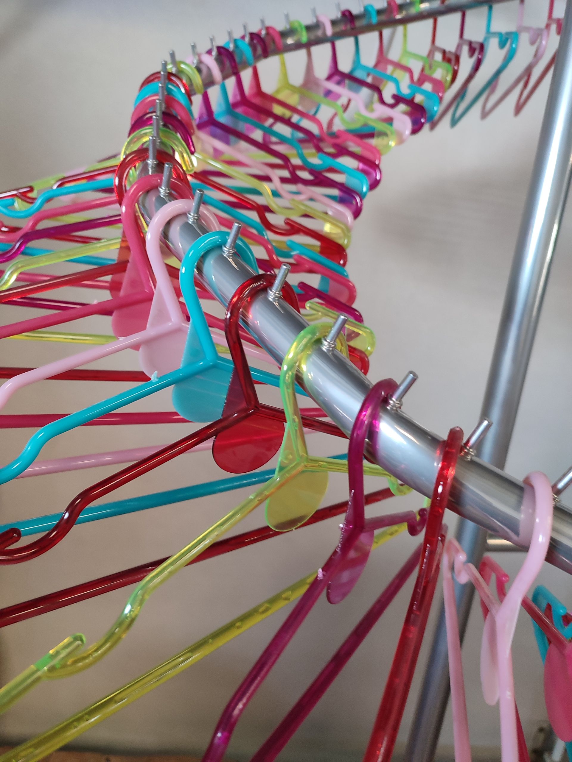 Perchas de plástico de colores agrupadas en un perchero plateado.