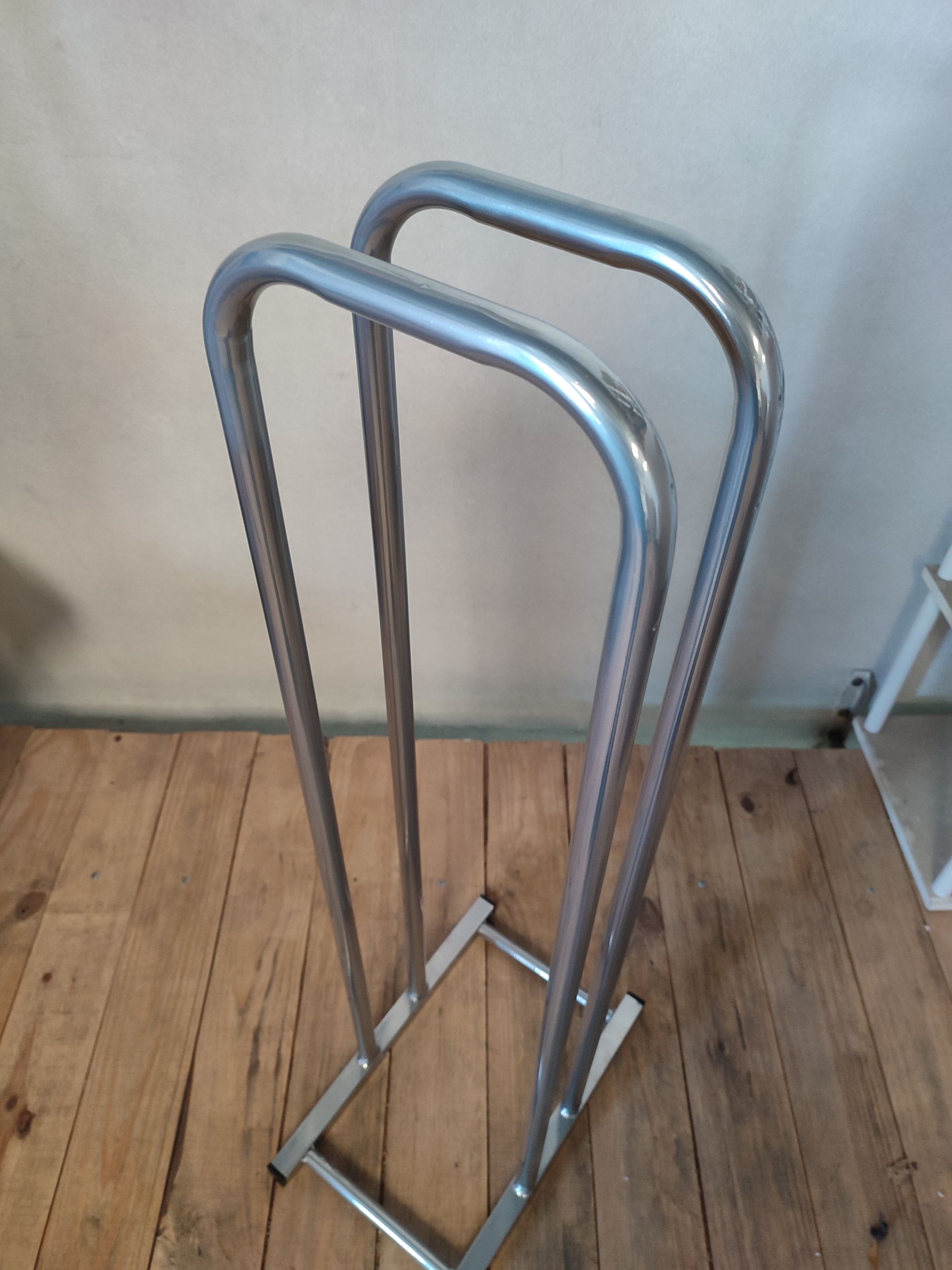 Un toallero de metal plateado con dos barras, colocado sobre un suelo de madera.