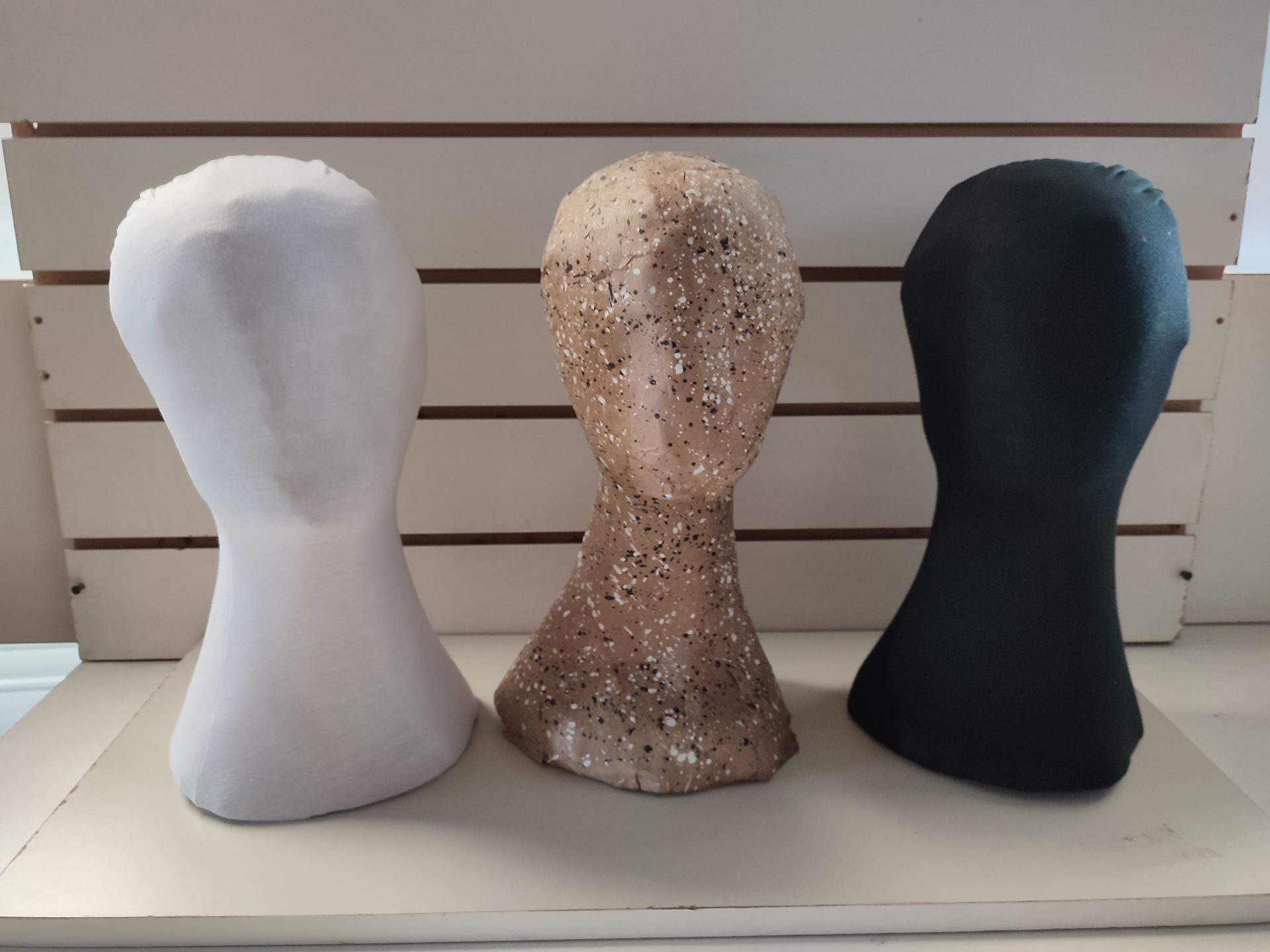 Tres cabezas de maniquí en color blanco, tostado moteado y negro, dispuestas en fila sobre un fondo de madera clara.