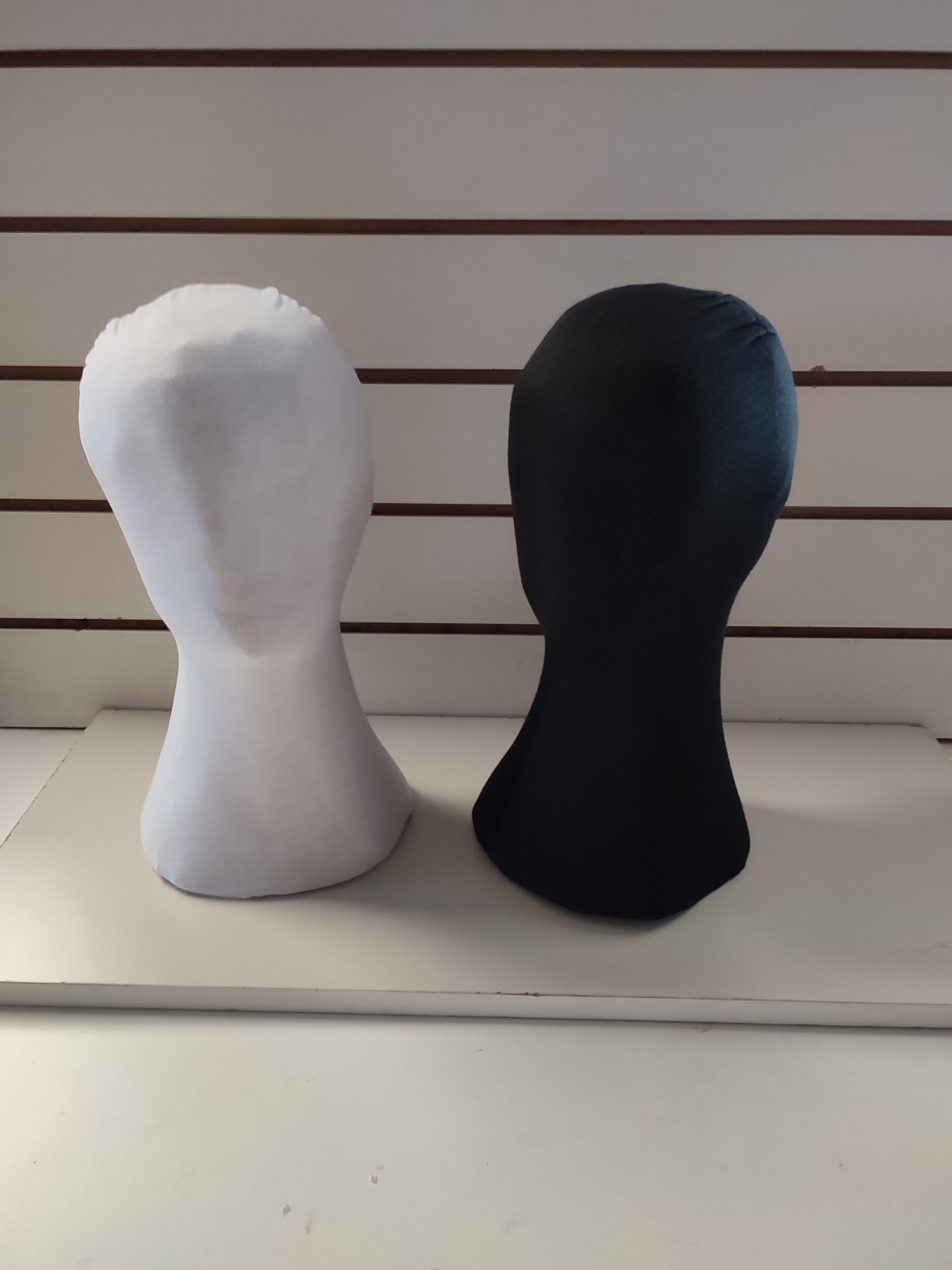 Cabezas de maniquí blancas y negras una al lado de la otra, contra un fondo de paneles blancos y marrones.