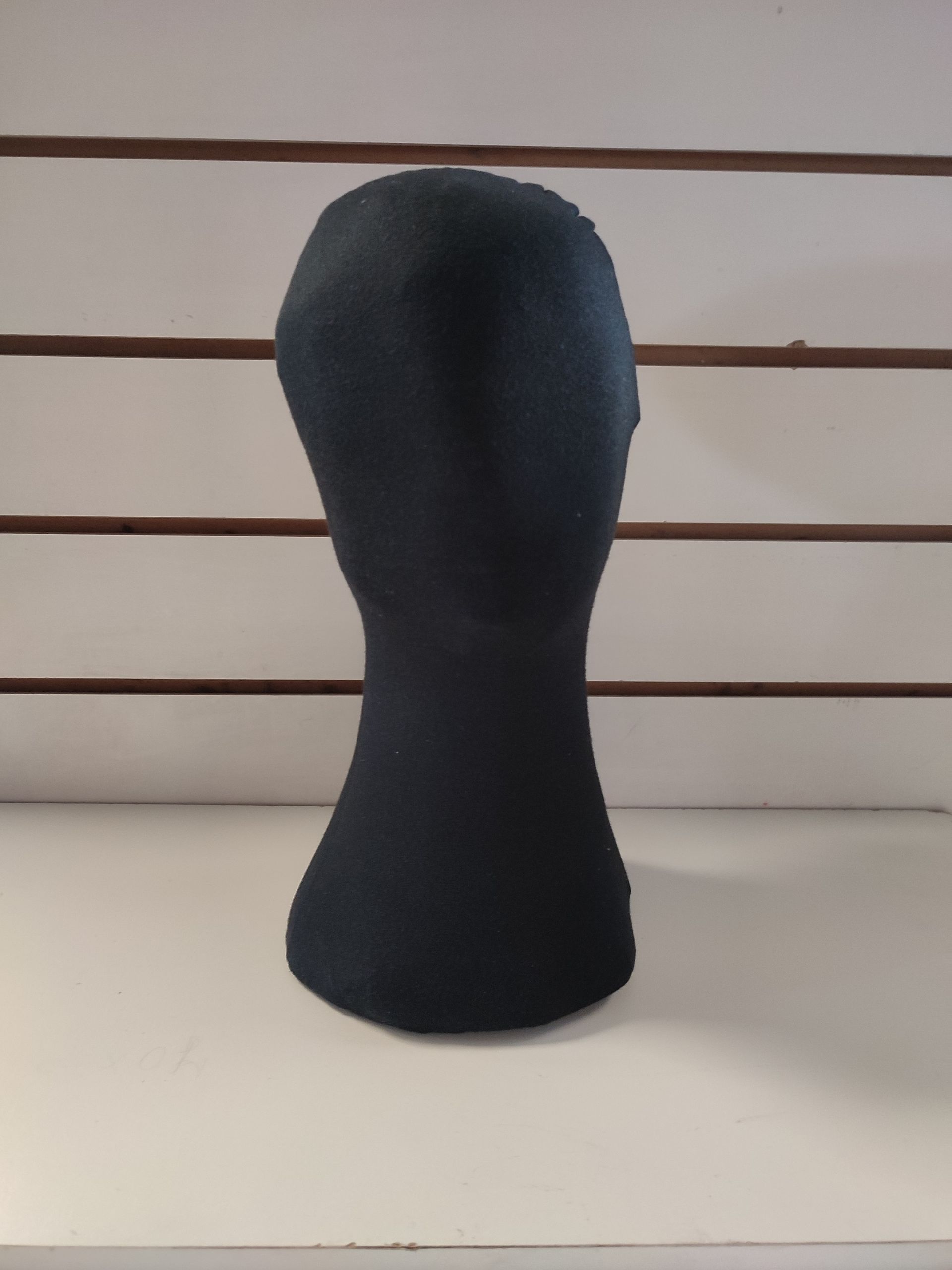 Cabeza de maniquí negro sobre un estante blanco contra una pared de listones blancos y marrones.