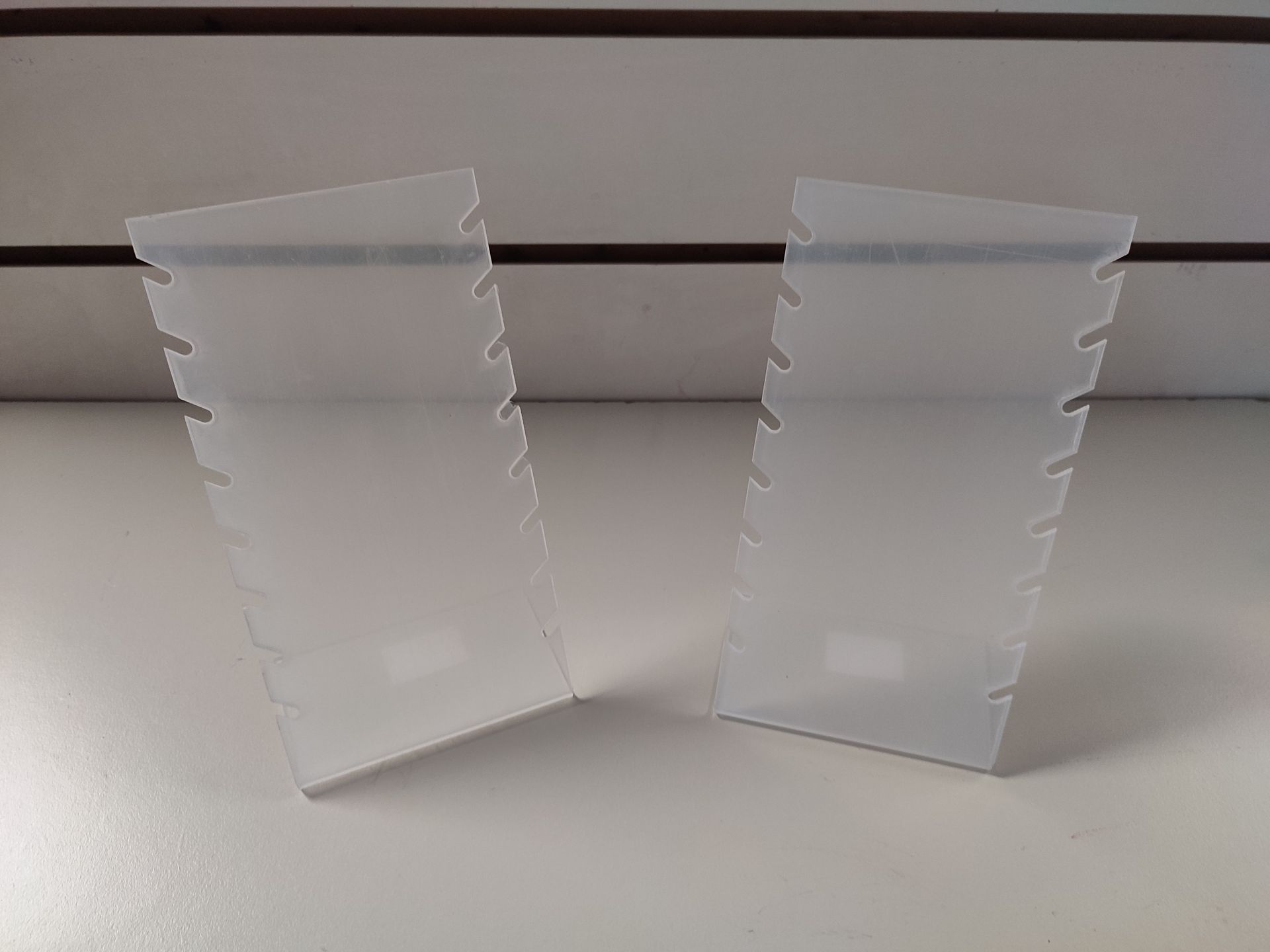 Dos expositores de collares de plástico transparente y en ángulo, con bordes dentados.