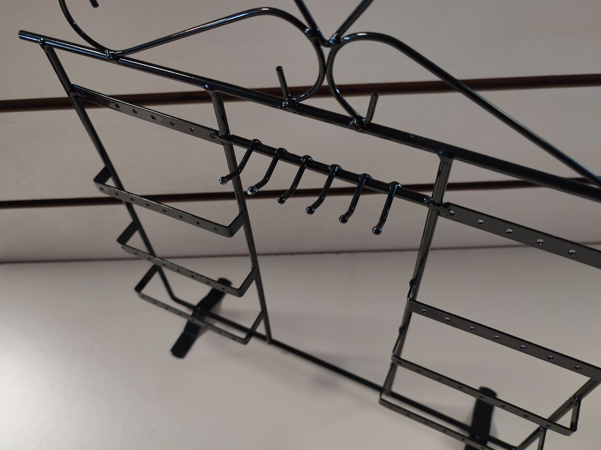 Vitrina de metal negro con ganchos y estantes, montada sobre pared blanca.