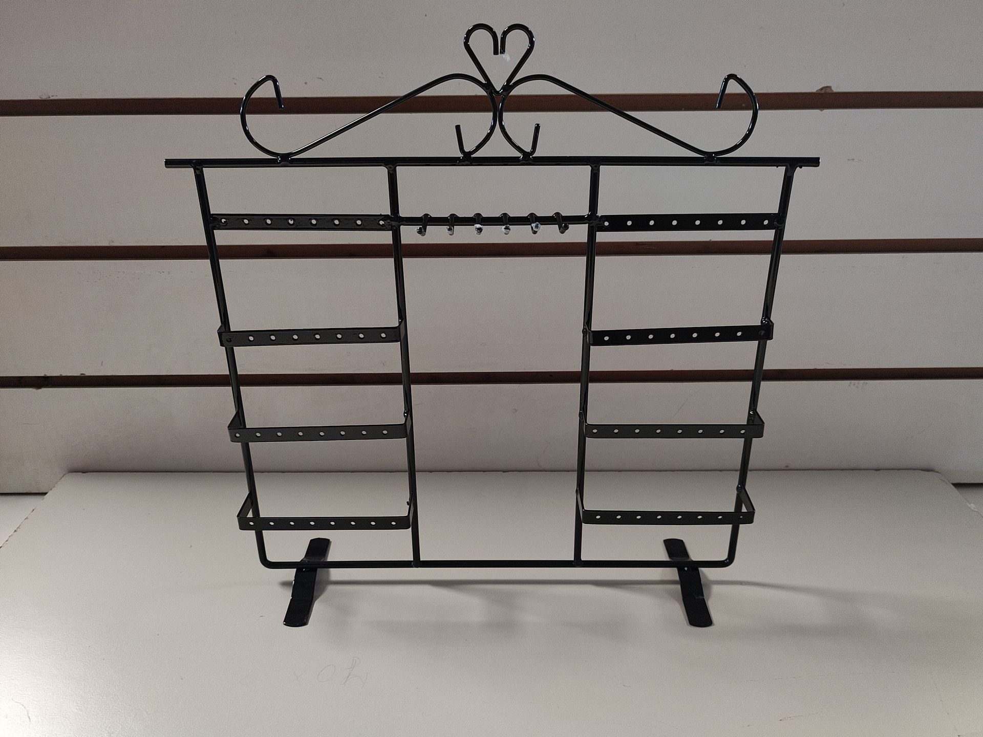 Exhibidor de aretes de metal negro con parte superior en forma de corazón, múltiples niveles y base de barra horizontal.
