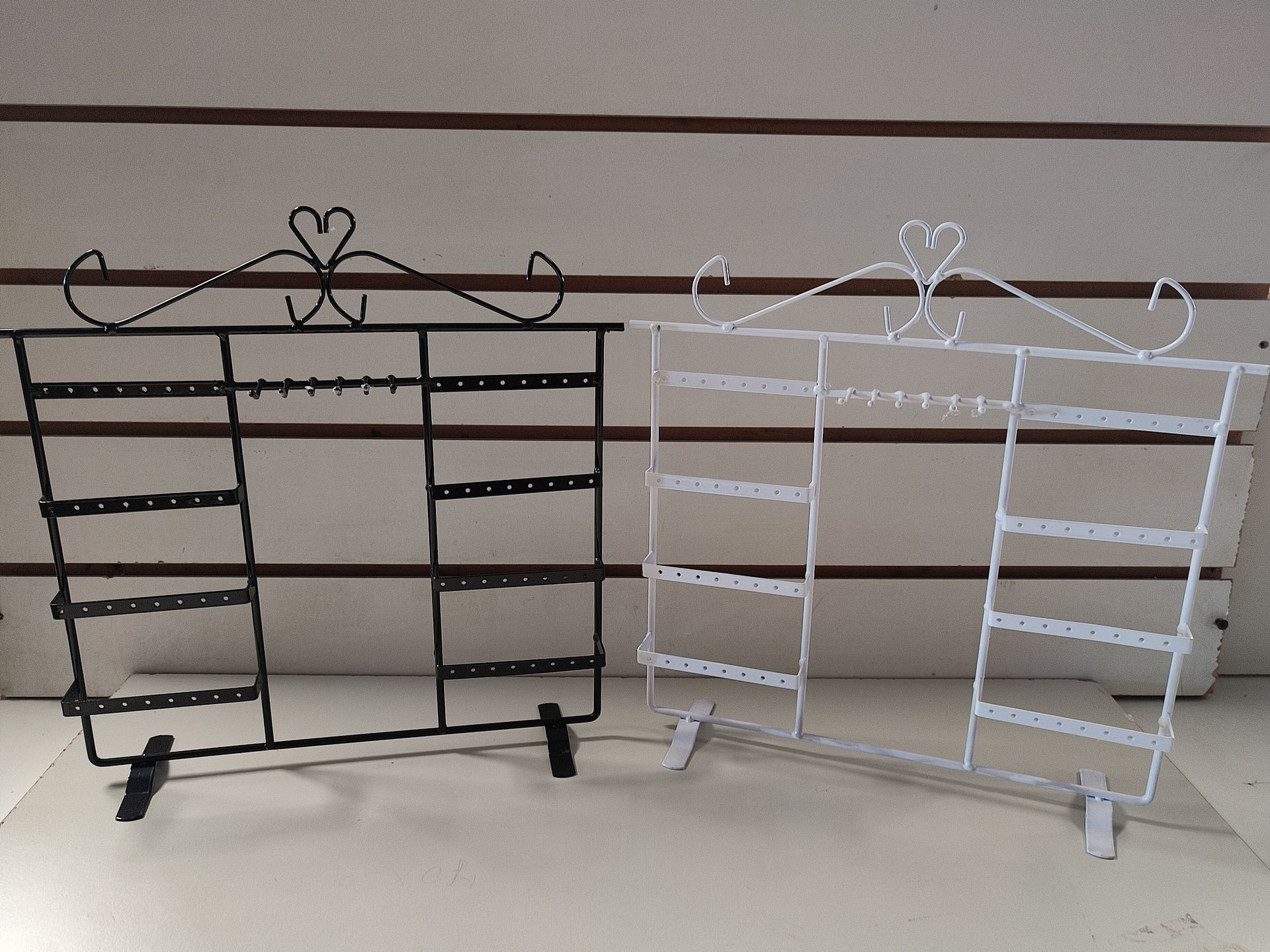 Exhibidores de pendientes de metal blanco y negro con volutas decorativas en un estante.