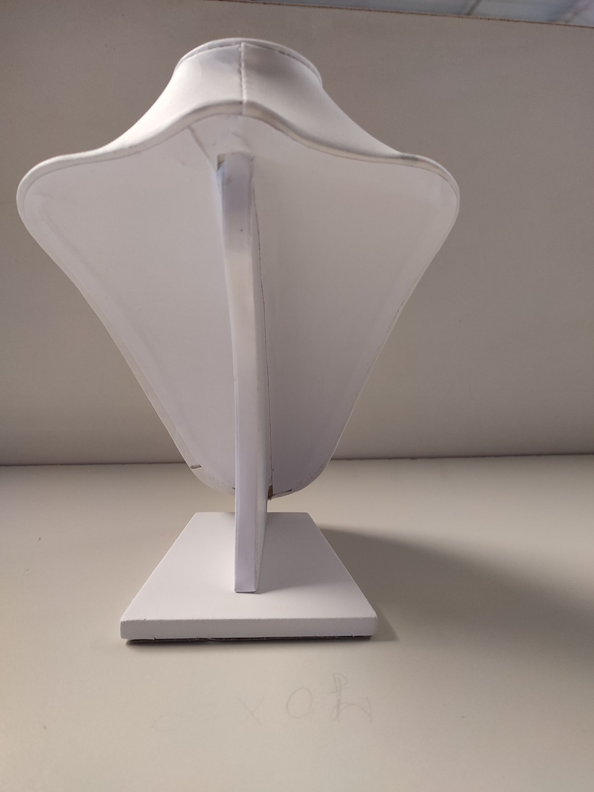 Expositor de collar blanco sobre superficie blanca, vista lateral.