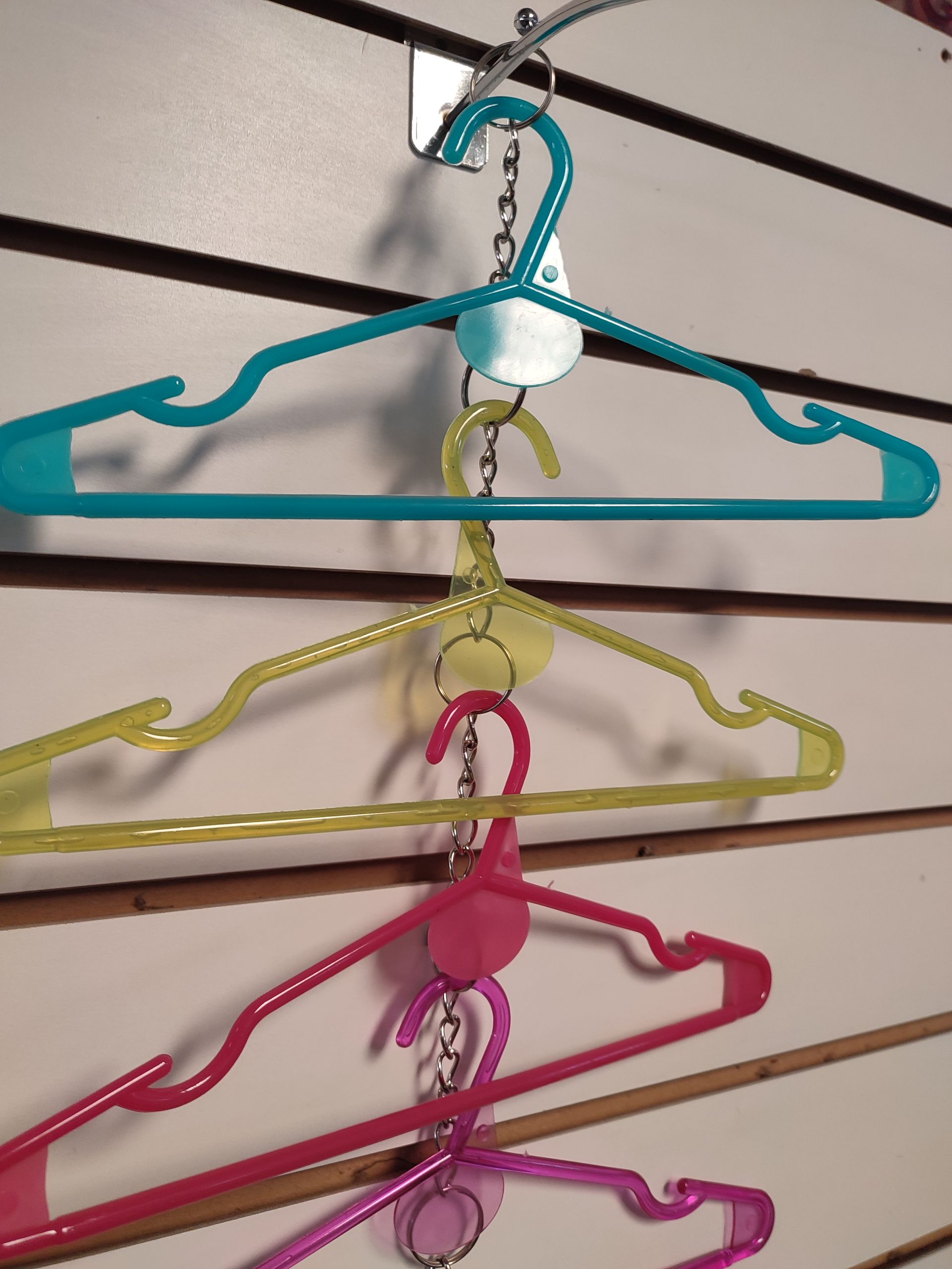 Tres perchas de plástico de colores unidas por una cadena, colgadas en una pared de listones.