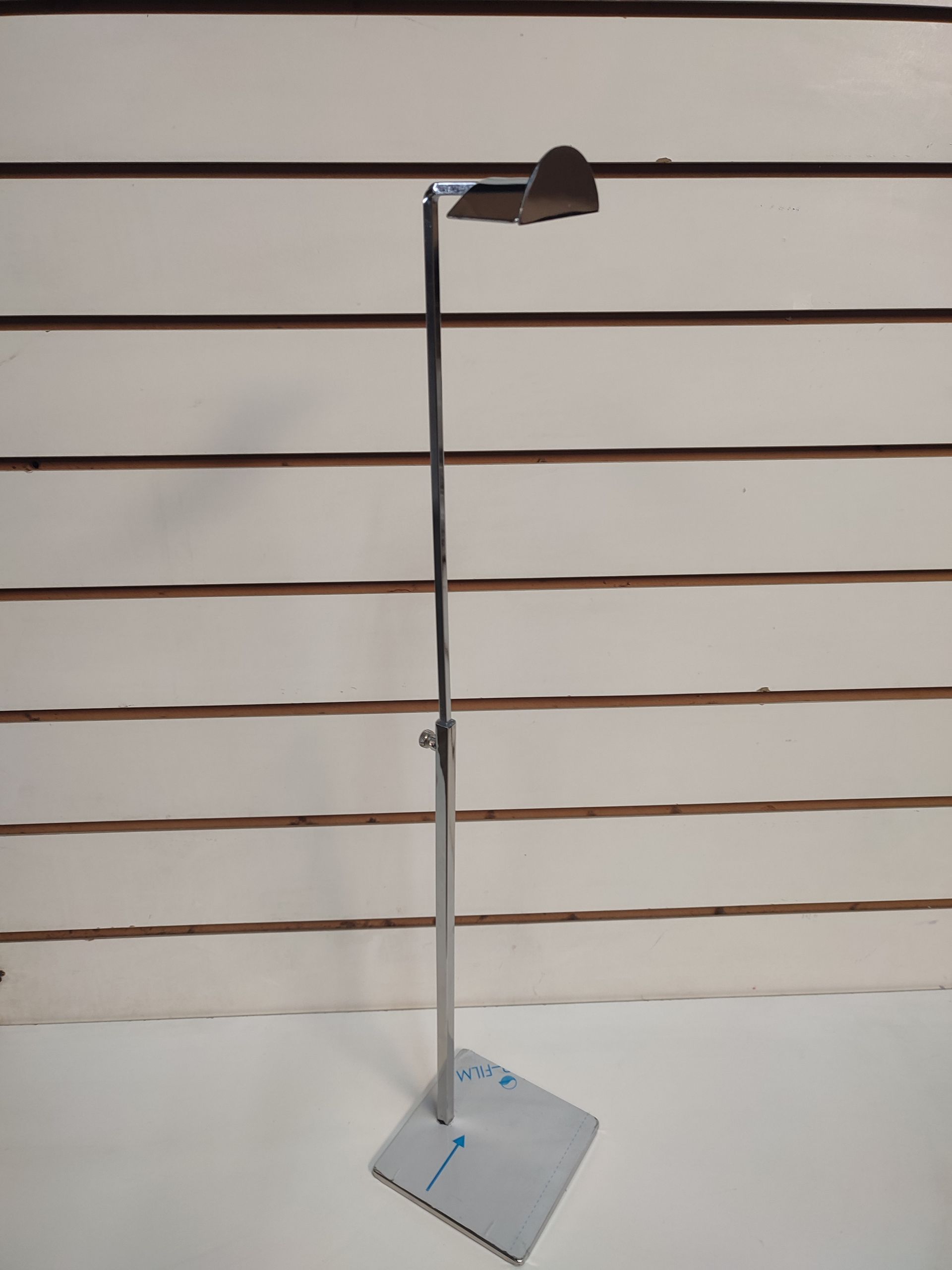 Expositor de sombreros metálico sobre base cuadrada, sobre fondo blanco de líneas horizontales.