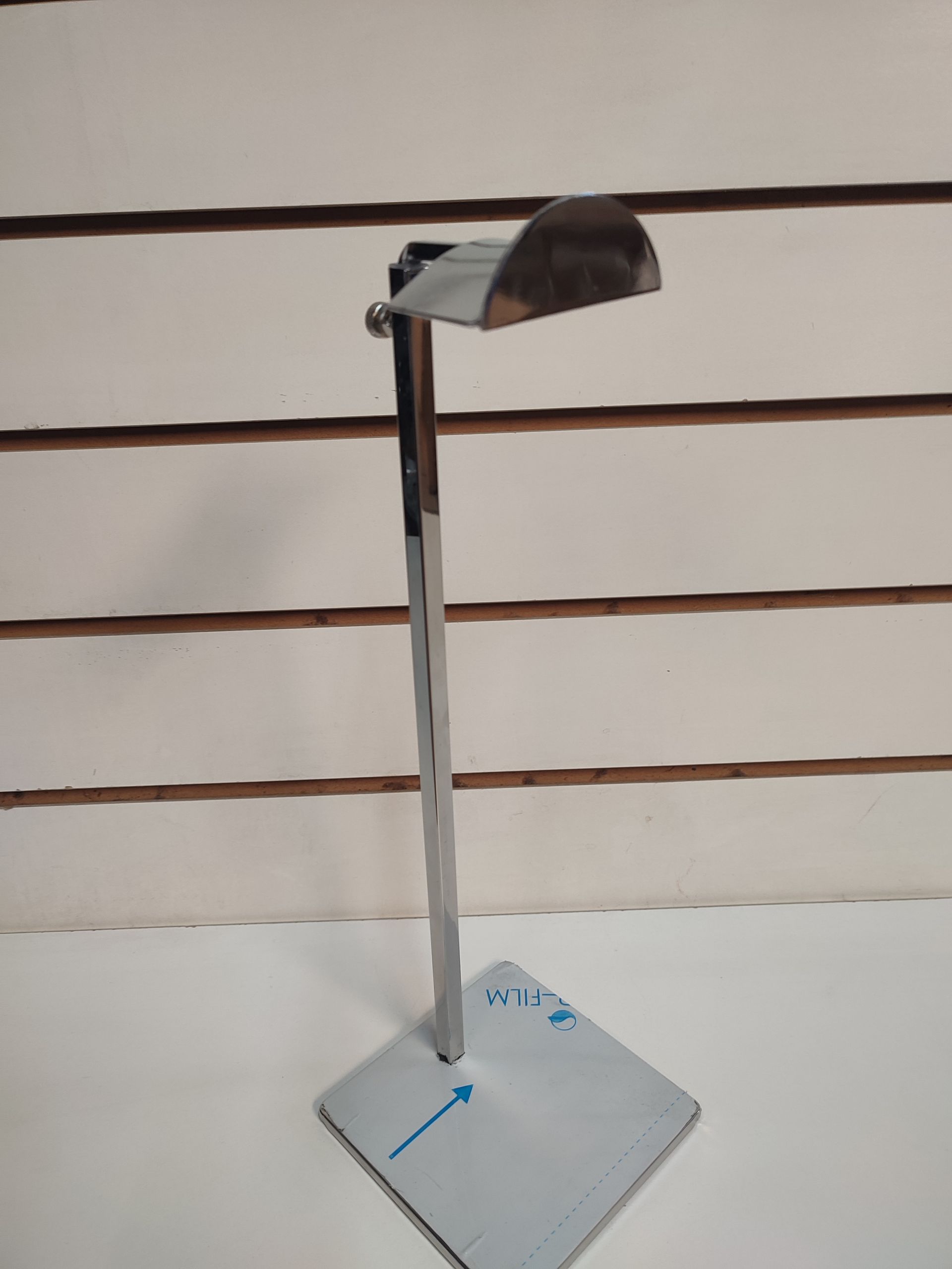 Un expositor de bolsos de acero inoxidable brillante sobre una base cuadrada, contra una pared de paneles blancos.