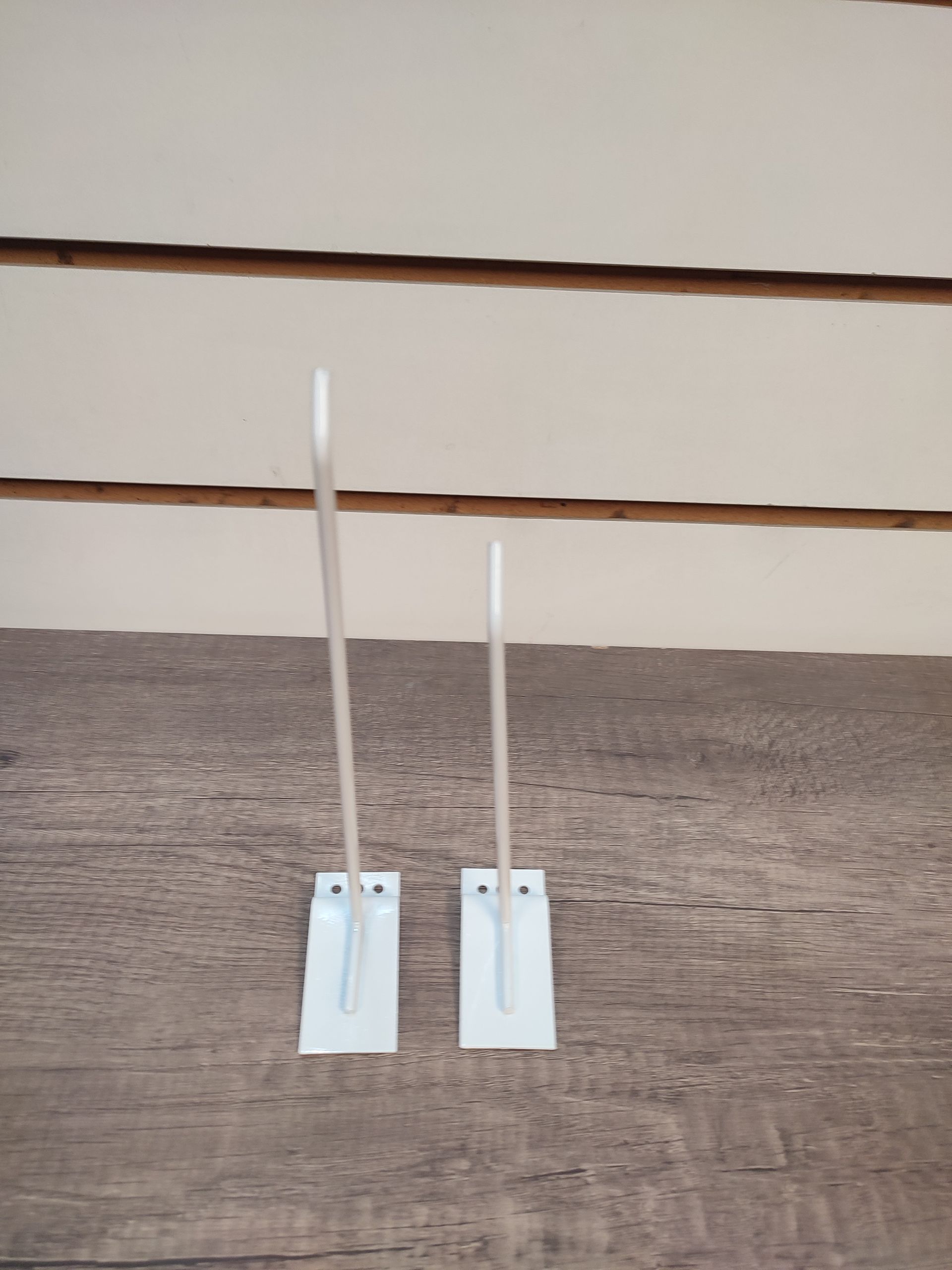 Dos porta carteles blancos sobre una superficie de madera, cada uno con un poste alto y delgado que se extiende hacia arriba.