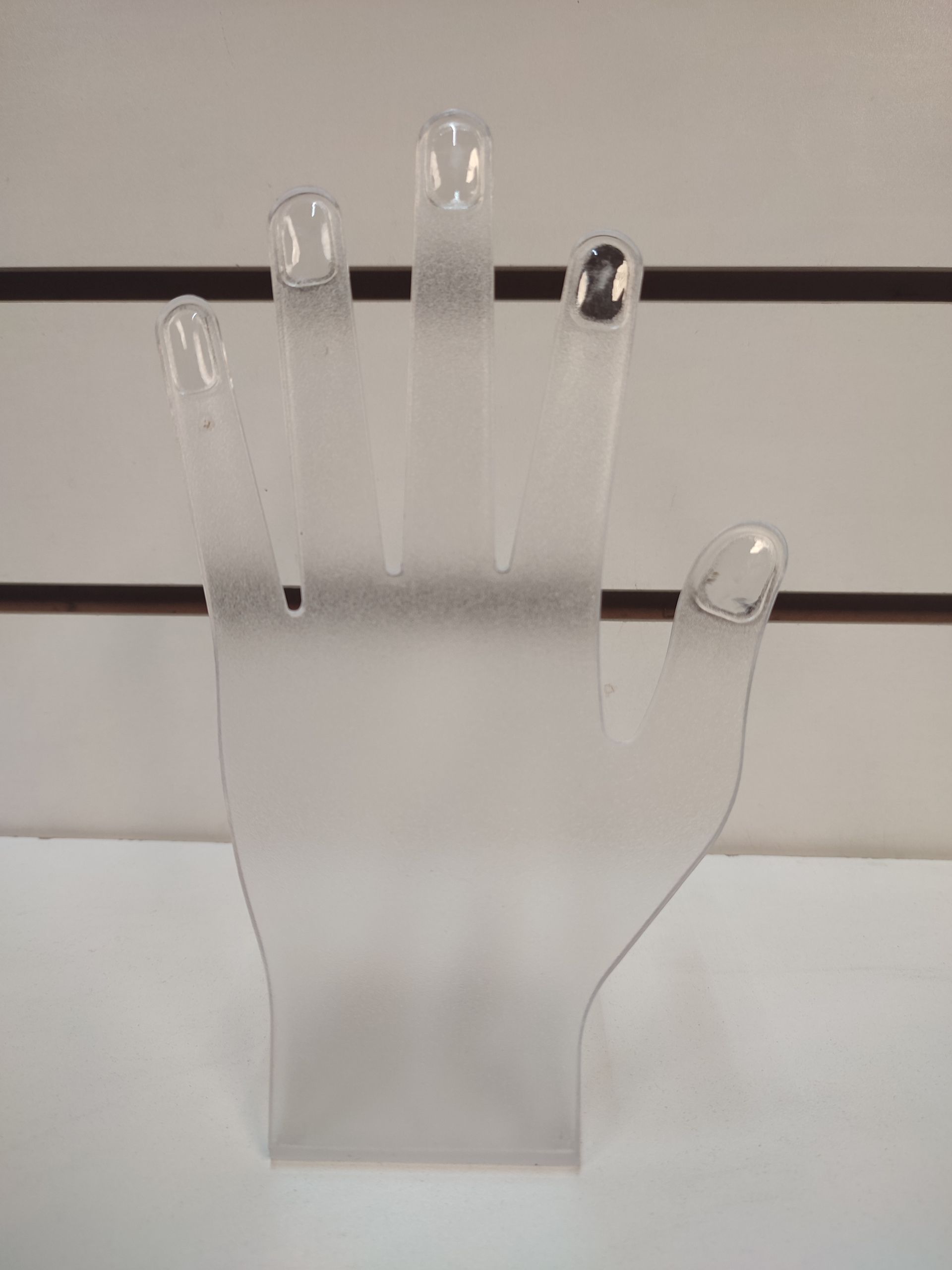 Expositor de joyas de plástico transparente en forma de mano con dedos extendidos.