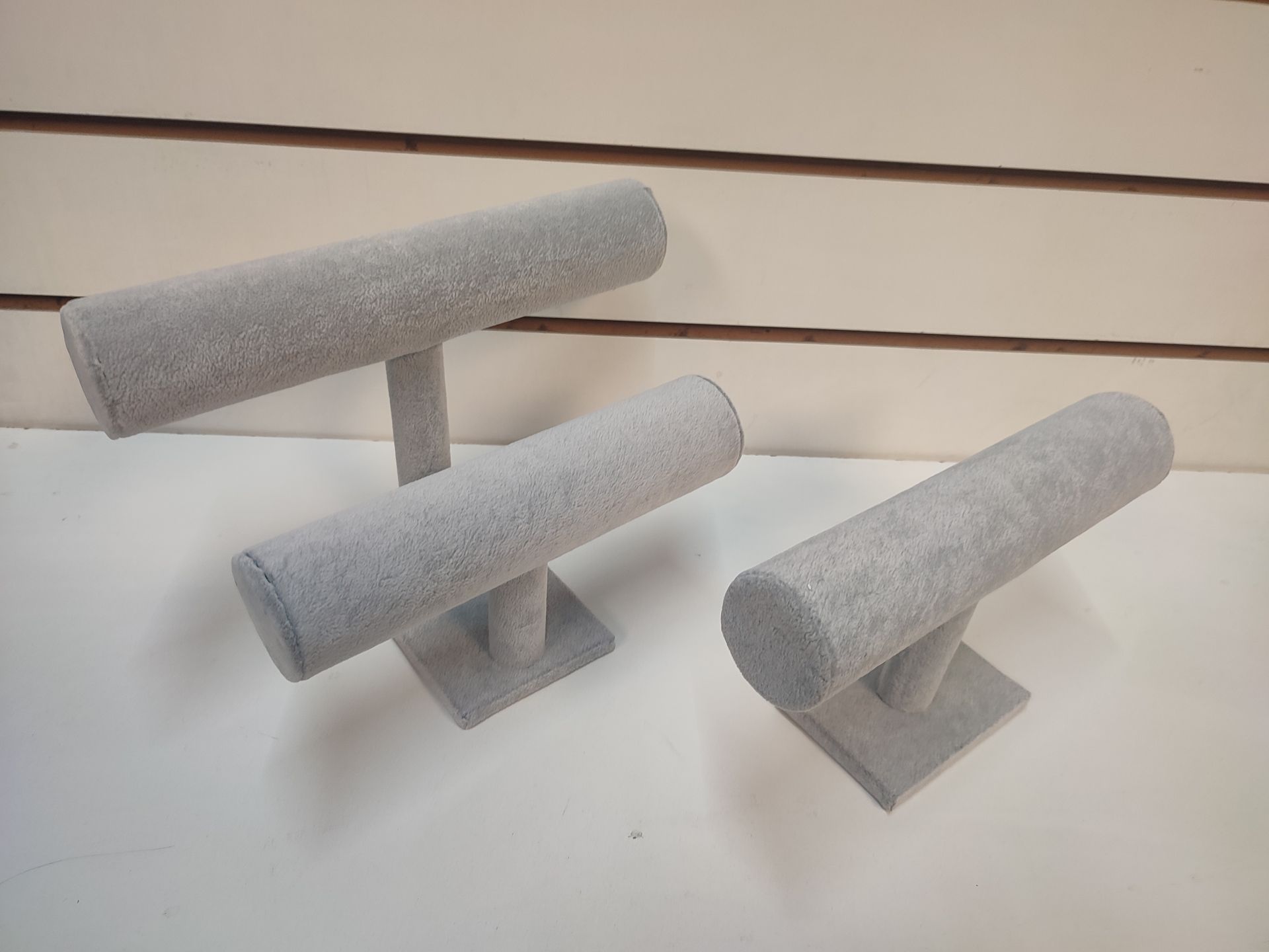 Tres expositores de joyas de terciopelo gris sobre una superficie blanca, con fondo rayado.