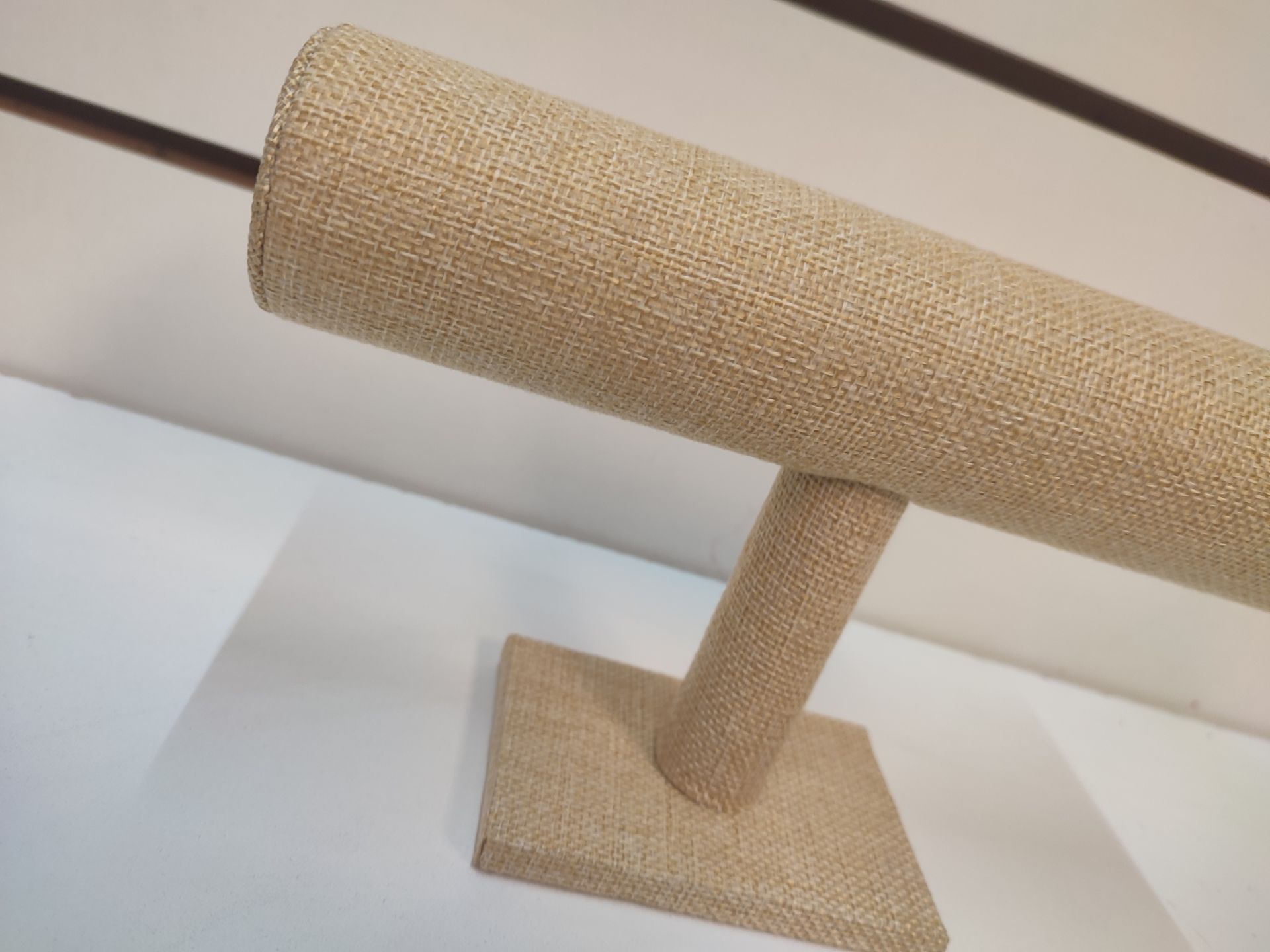 Expositor de joyas de arpillera beige con barra horizontal.