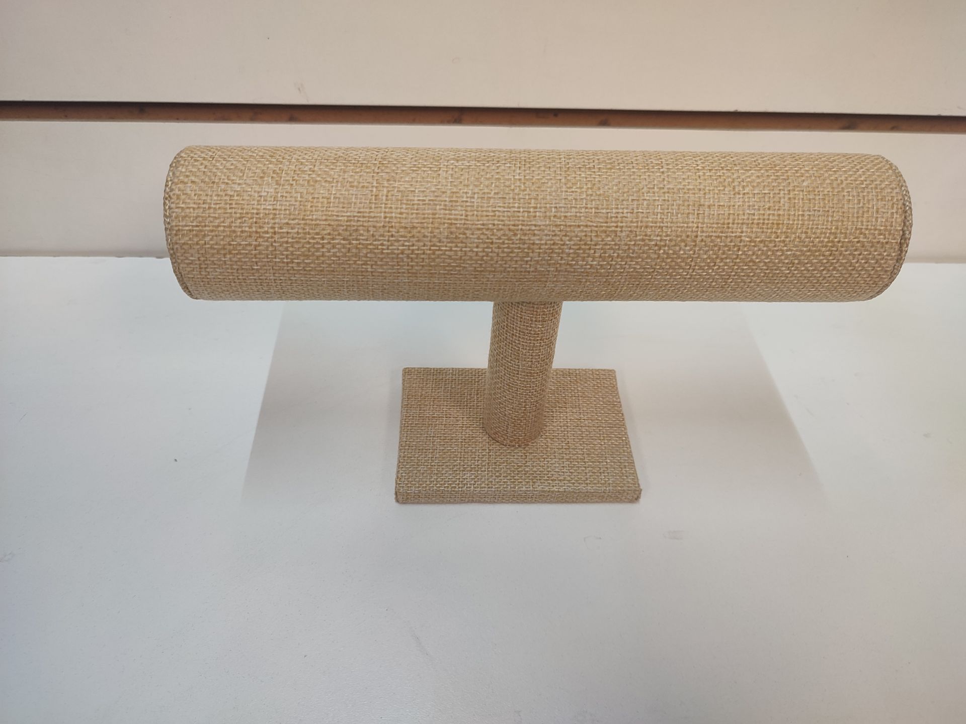 Expositor de pulseras de arpillera color canela sobre superficie blanca.