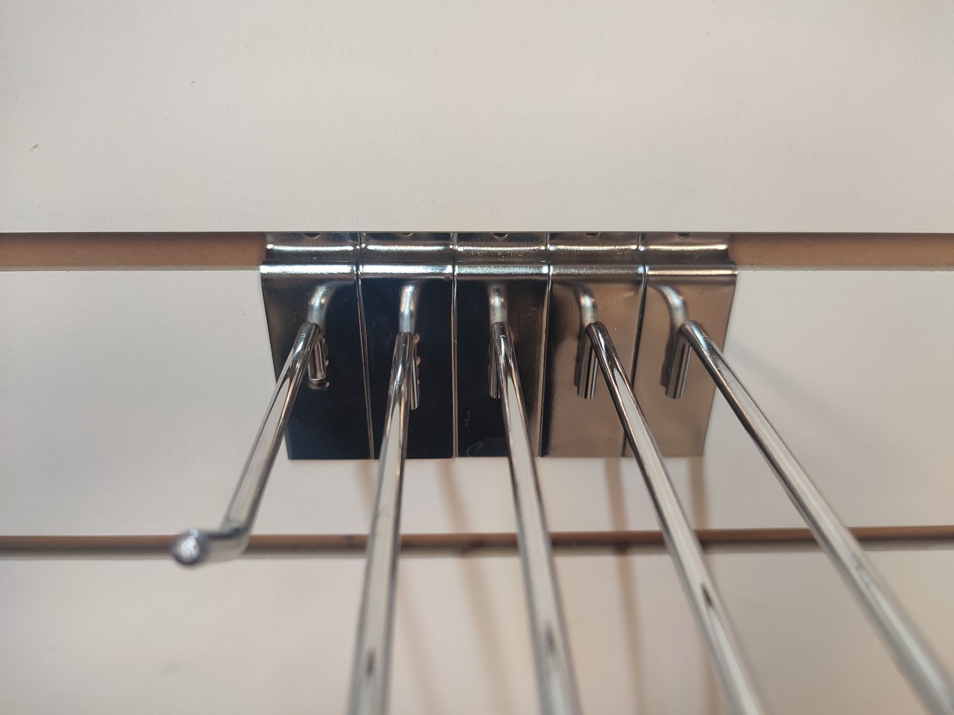 Ganchos de exhibición de metal fijados a una pared de listones de color blanco.