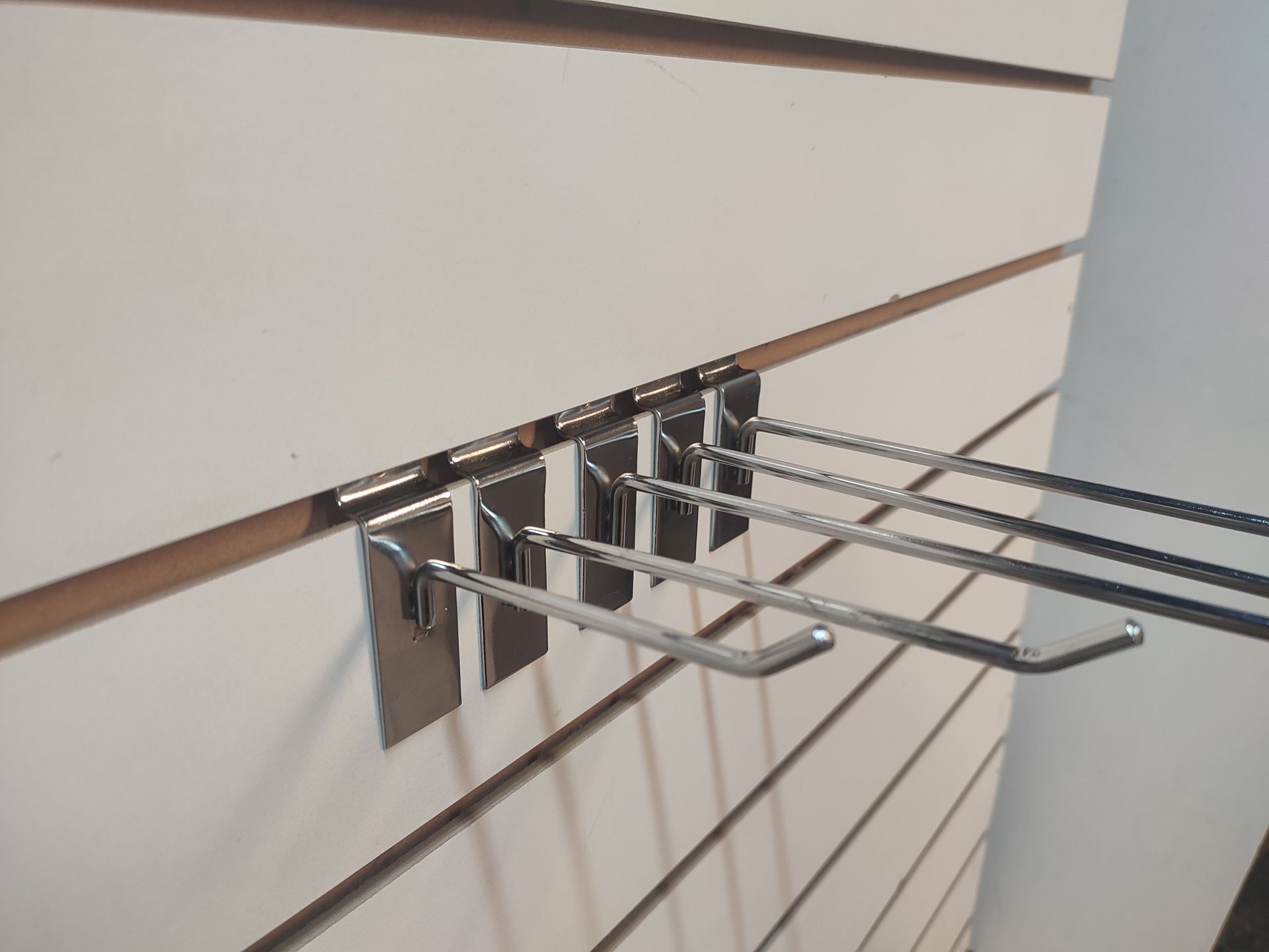 Ganchos de exhibición de metal sobre una pared de listones blancos, para exhibición minorista.