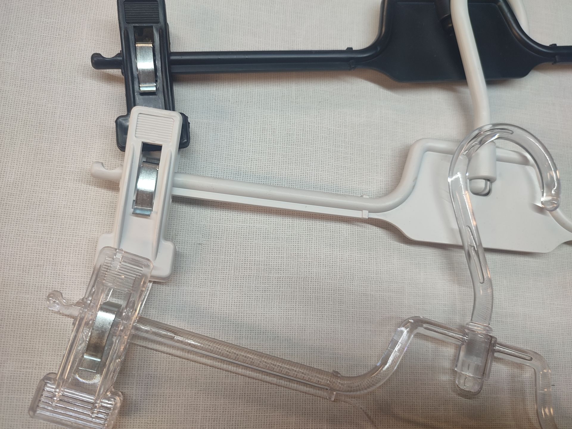 Tres perchas de ropa diferentes: de plástico negro, blanco y transparente, apiladas.