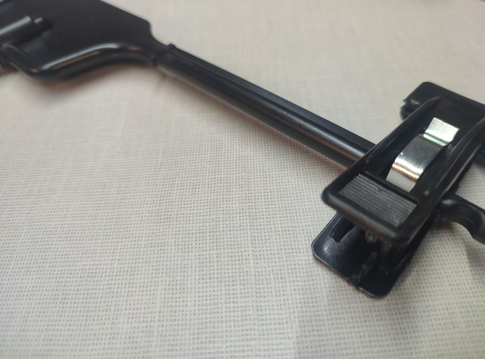 Percha de plástico negra con clips que descansa sobre una superficie blanca texturizada.