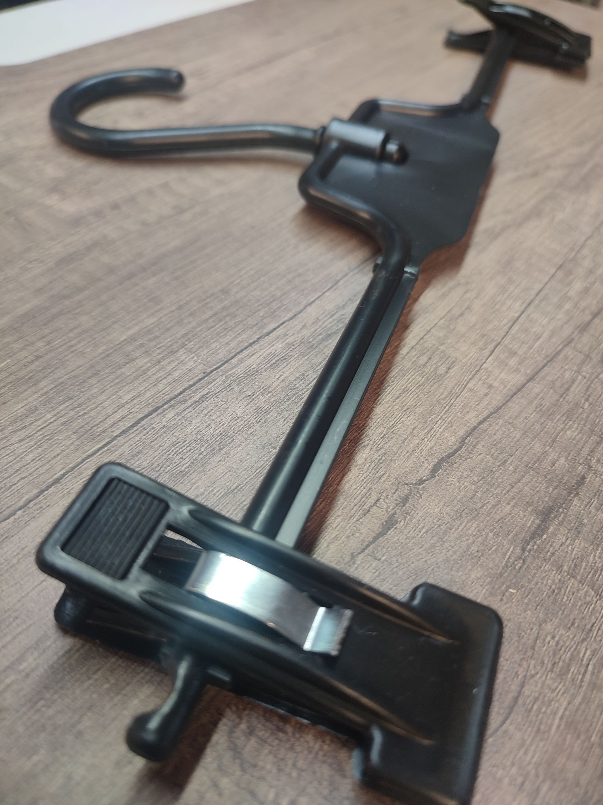 Percha para pantalones de color negro, con pinzas y gancho, sobre superficie marrón.