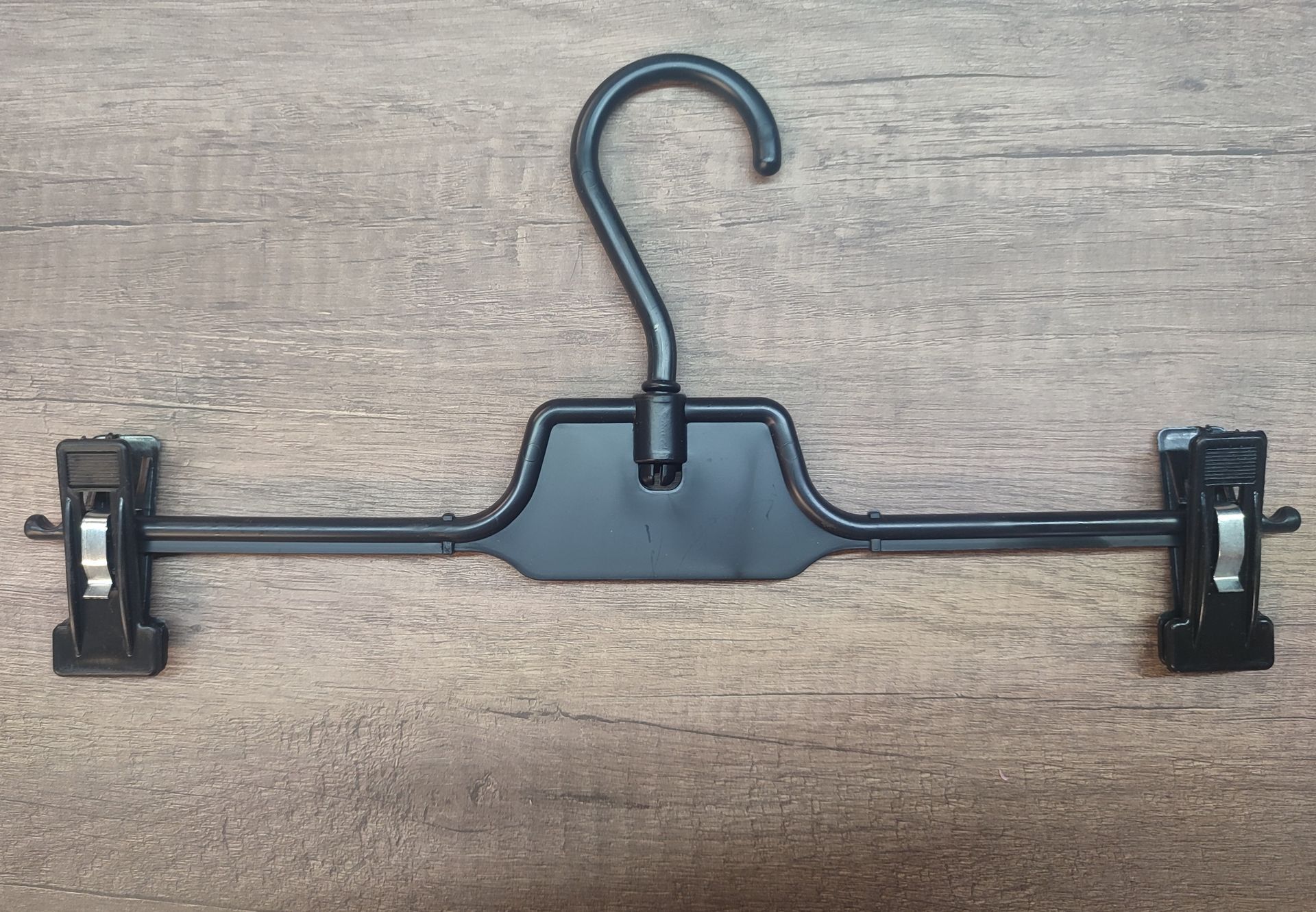 Percha de ropa negra con pinzas, sobre superficie de madera.