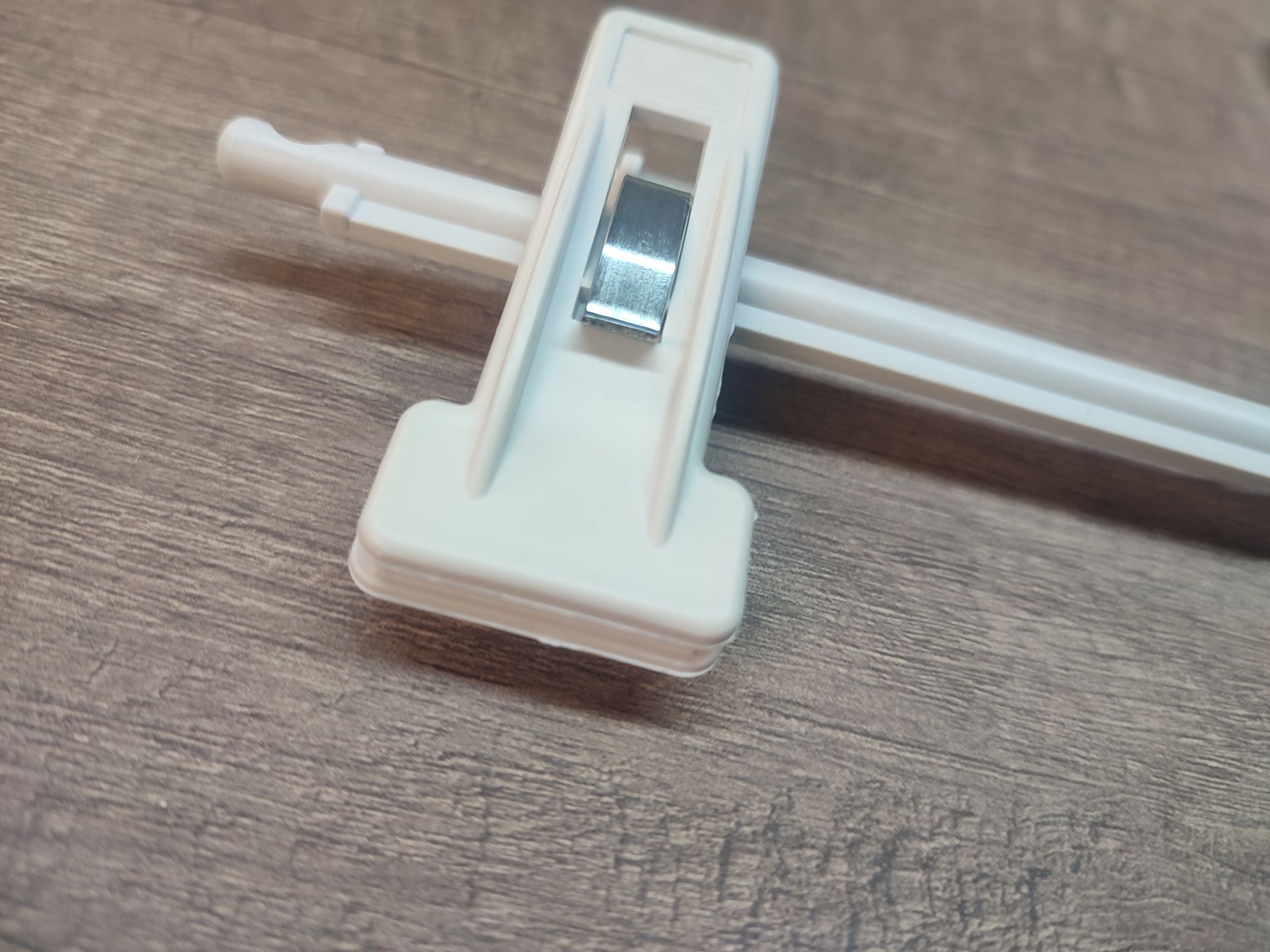 Varilla ciega de plástico blanco con clip de metal sobre superficie con veta de madera.