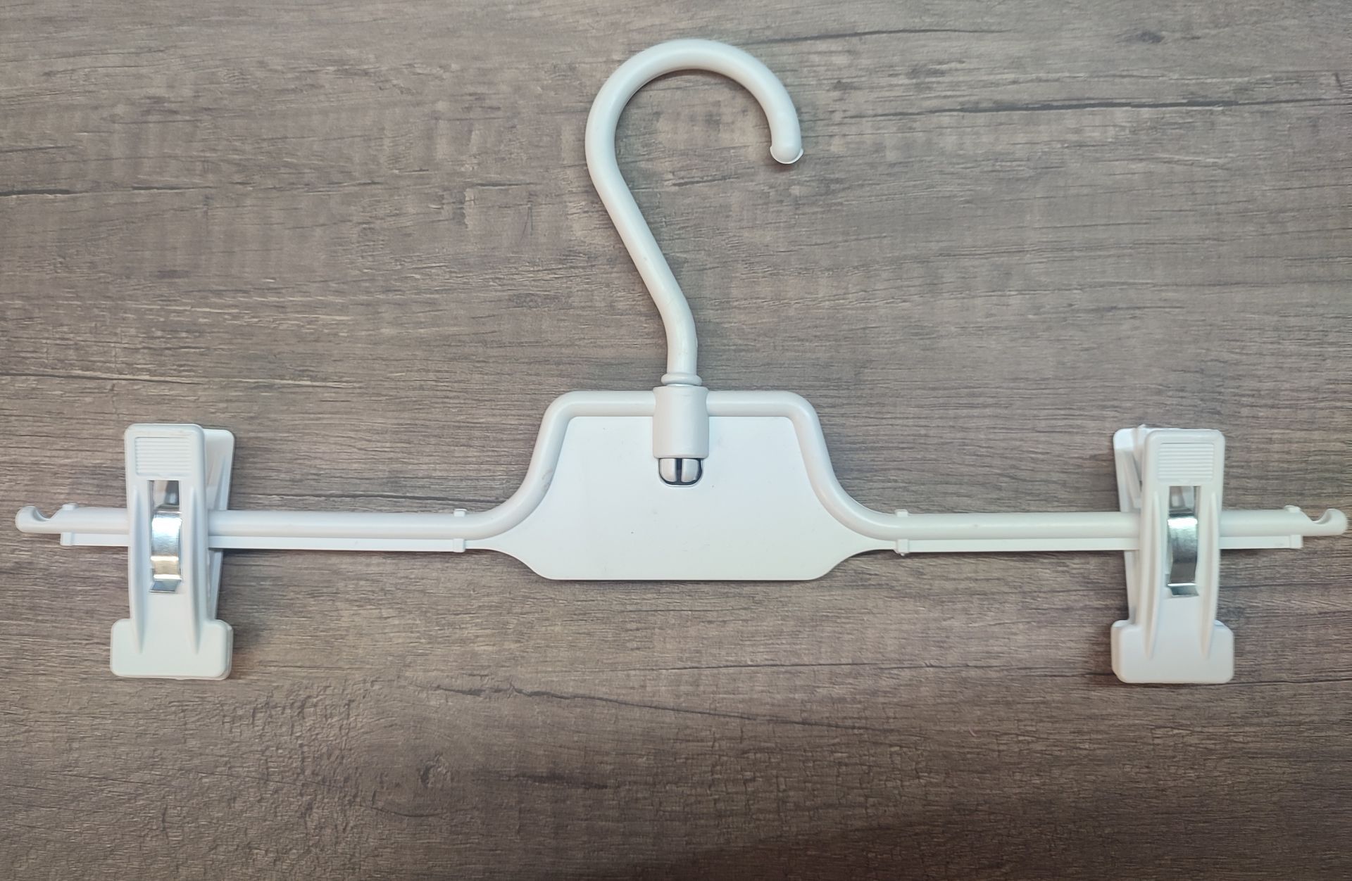 Percha de plástico blanca con pinzas para pantalones, sobre superficie de madera.