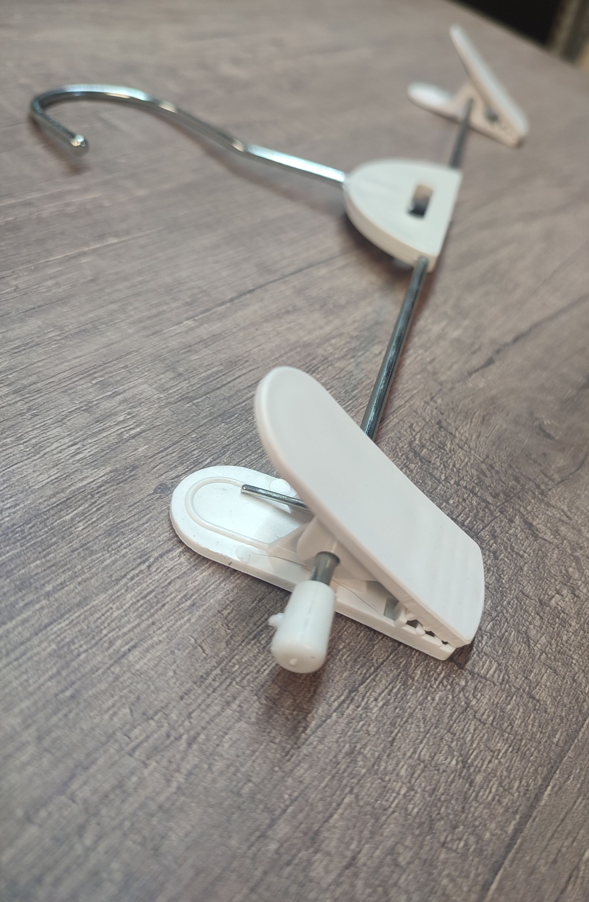 Percha para pantalones de plástico blanco con pinzas ajustables sobre superficie de madera.
