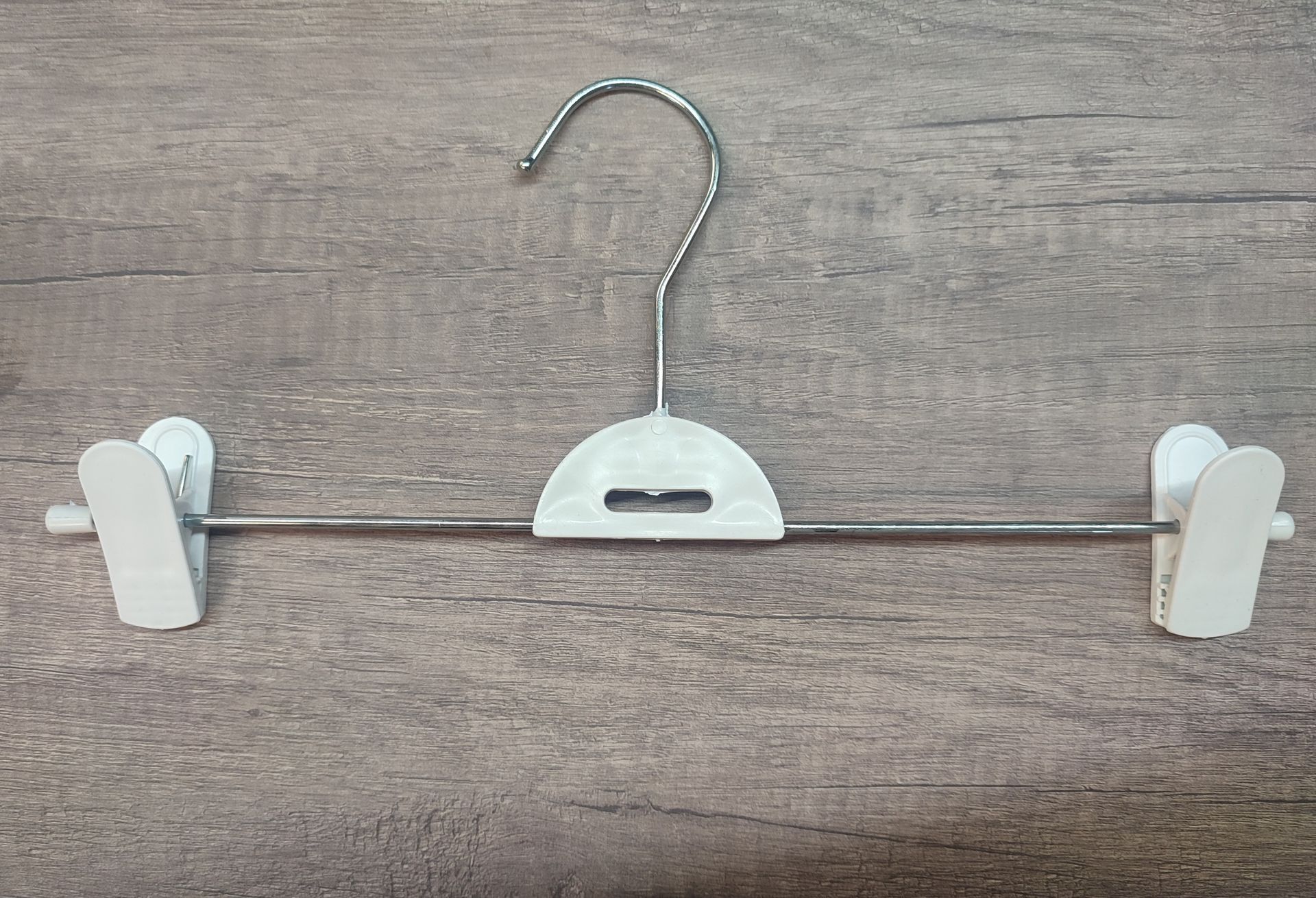 Percha para pantalones de color blanco y metal sobre superficie imitación madera.