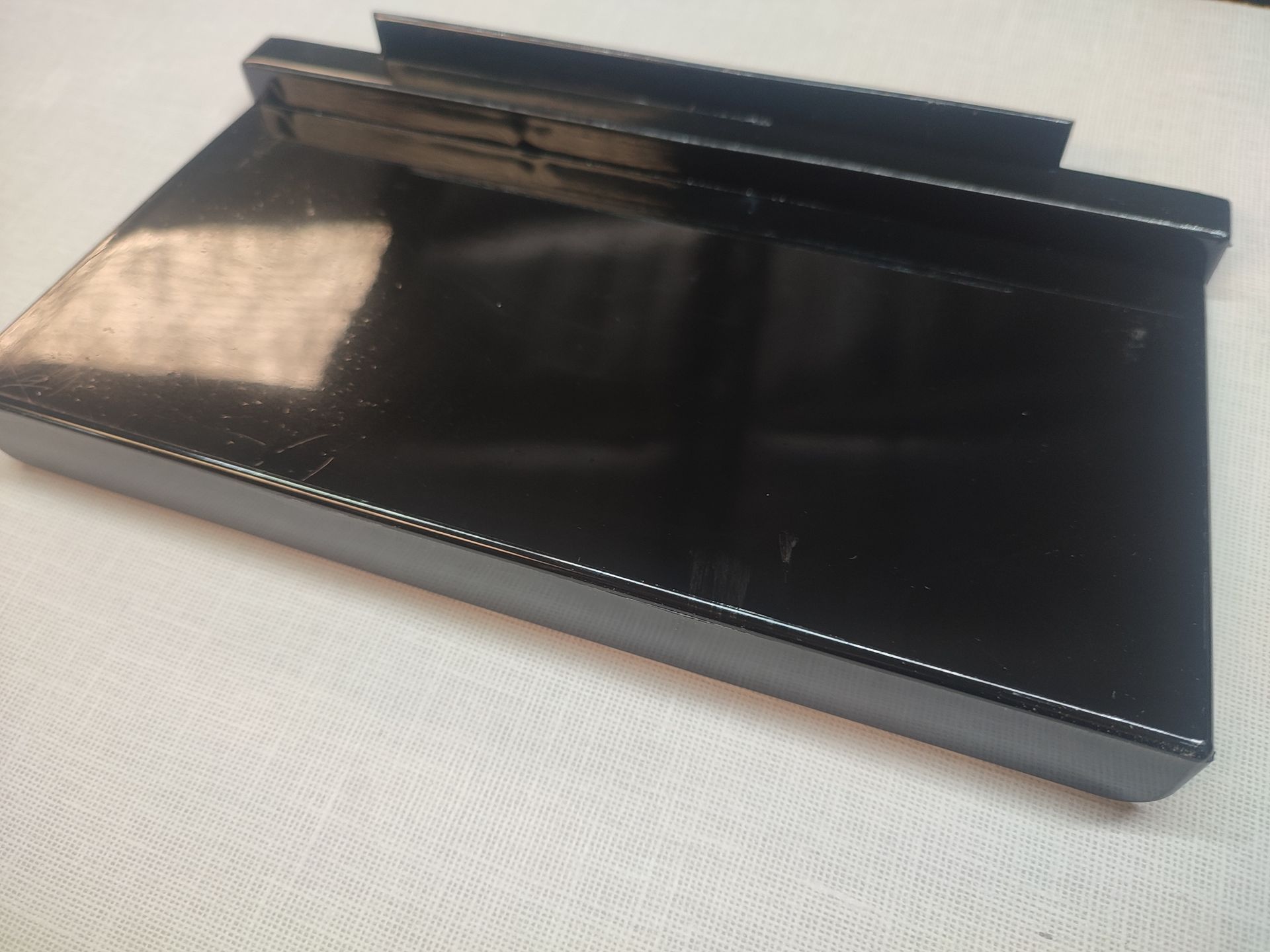 Bandeja rectangular negra con bordes elevados y sección superior; sobre superficie blanca.