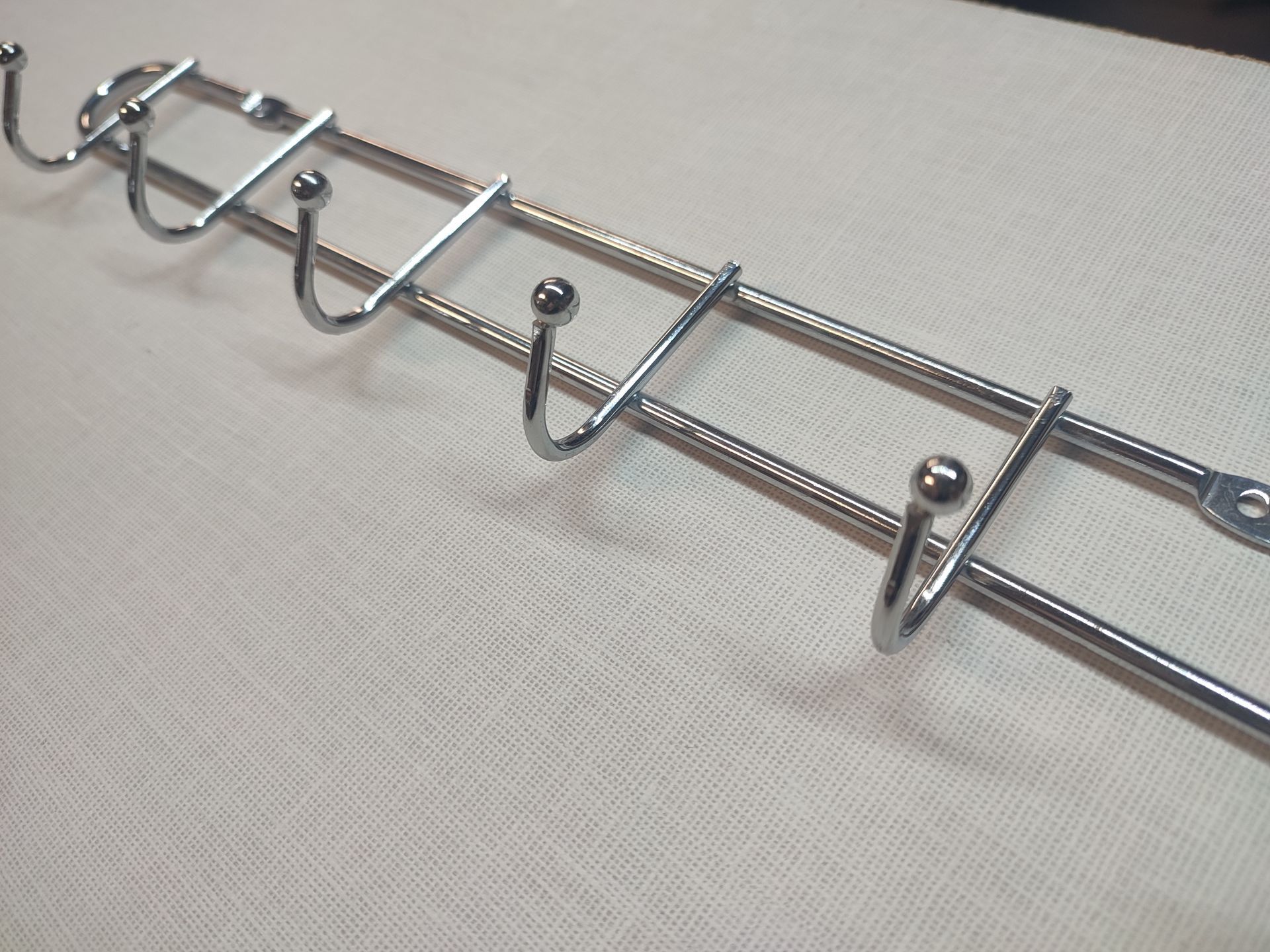 Perchero de pared de metal plateado con seis ganchos sobre una superficie blanca.