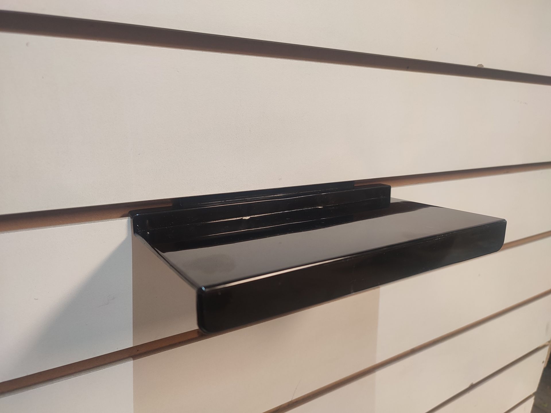 Estante negro fijado a una pared ranurada de color blanco.