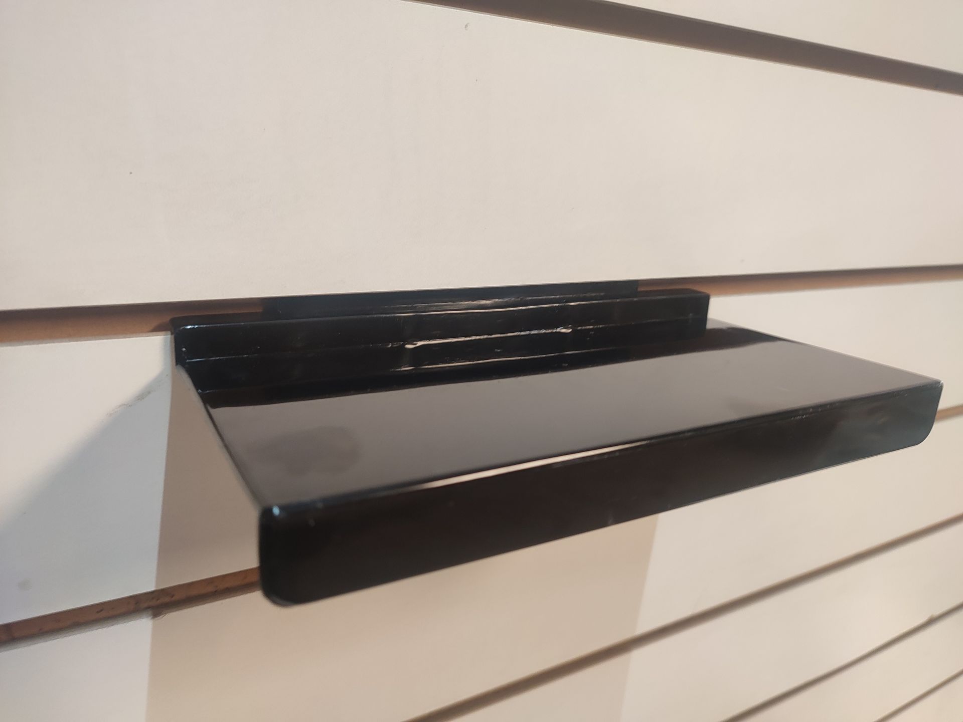 Estante flotante negro montado sobre pared de listones blancos.