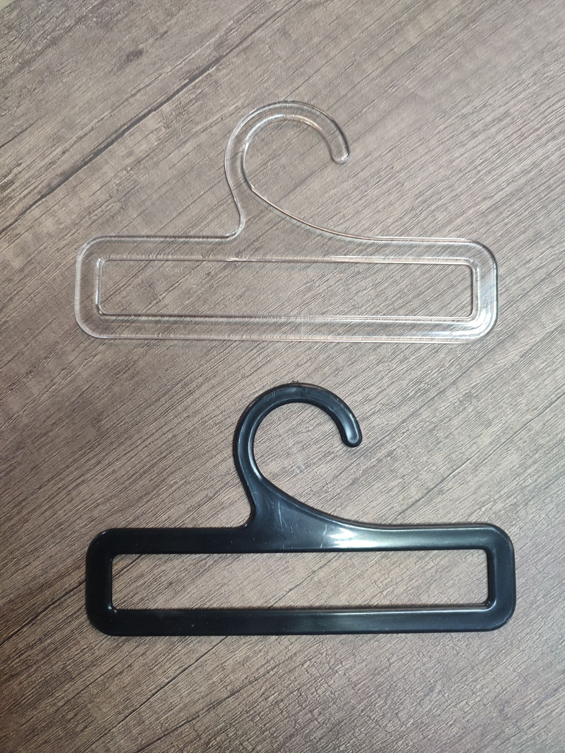 Dos perchas de plástico para cinturones, una transparente y otra negra, sobre una superficie de madera.