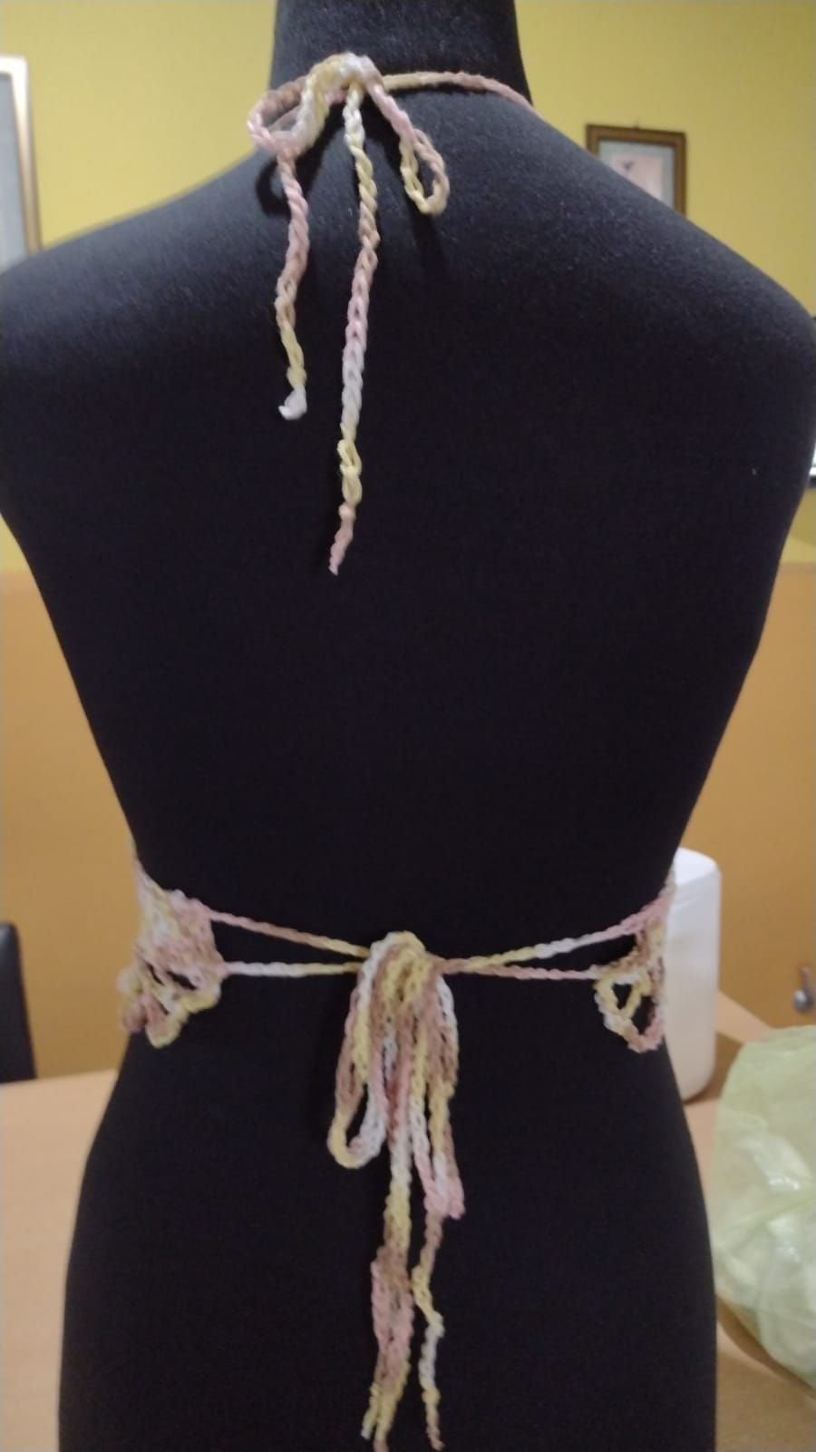 Parte posterior de un top de crochet color beige, atado al cuello y a la cintura sobre un maniquí negro.
