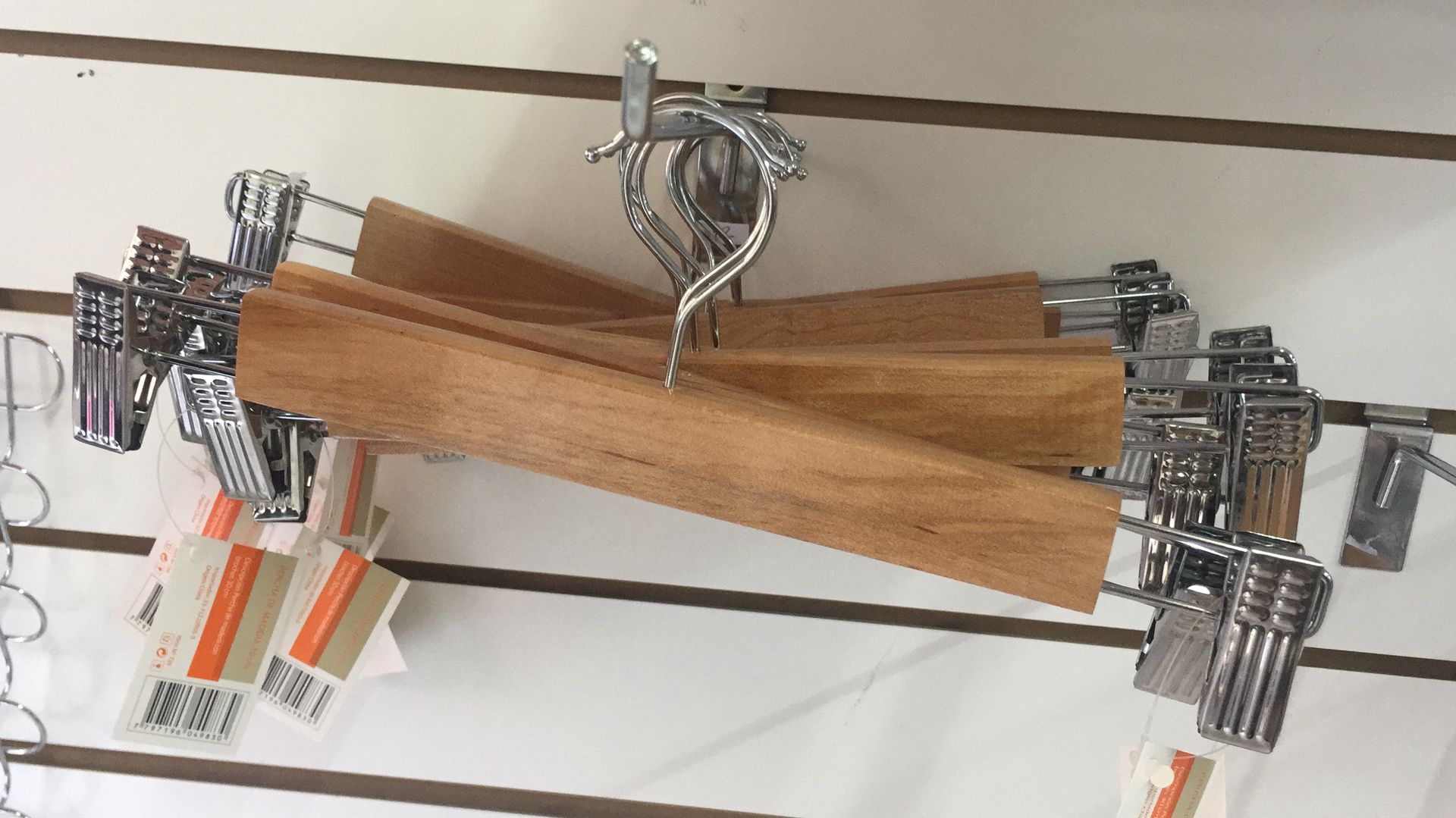 Perchas de madera para pantalones con pinzas metálicas colgadas en una vitrina de pared.