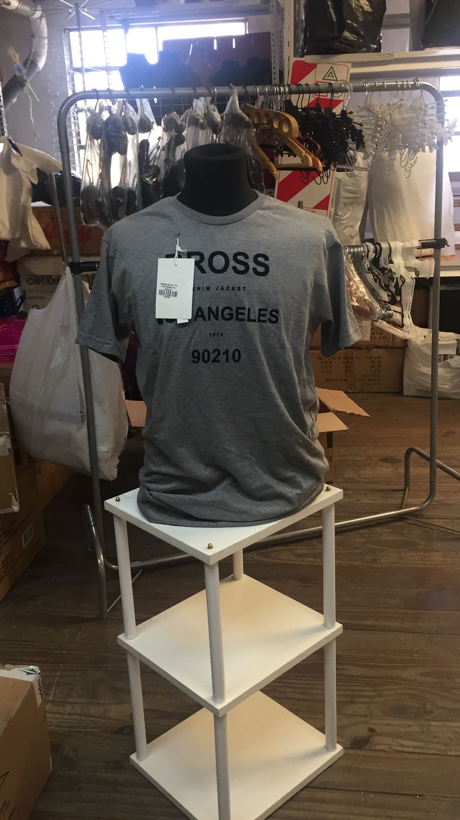 Camiseta gris en un expositor blanco de tres niveles; el texto en la camiseta dice 