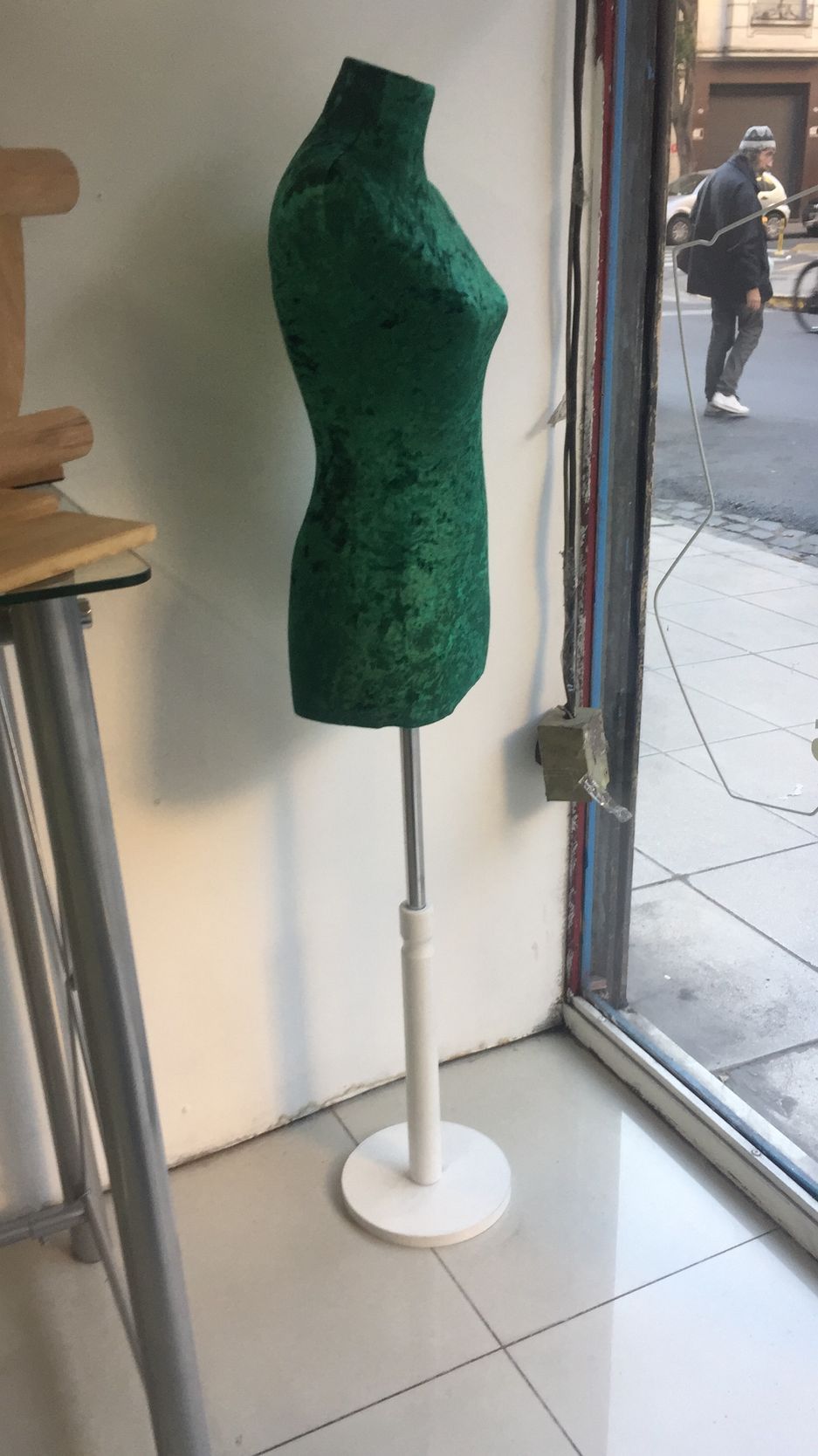 Maniquí de vestido con lentejuelas verdes sobre un soporte blanco, en el interior junto a una ventana.