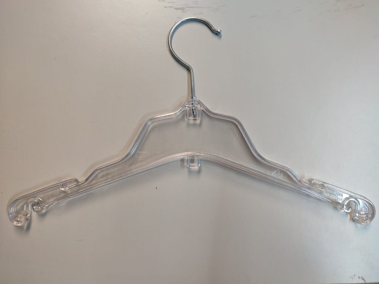 Percha de ropa de plástico transparente con gancho de metal.