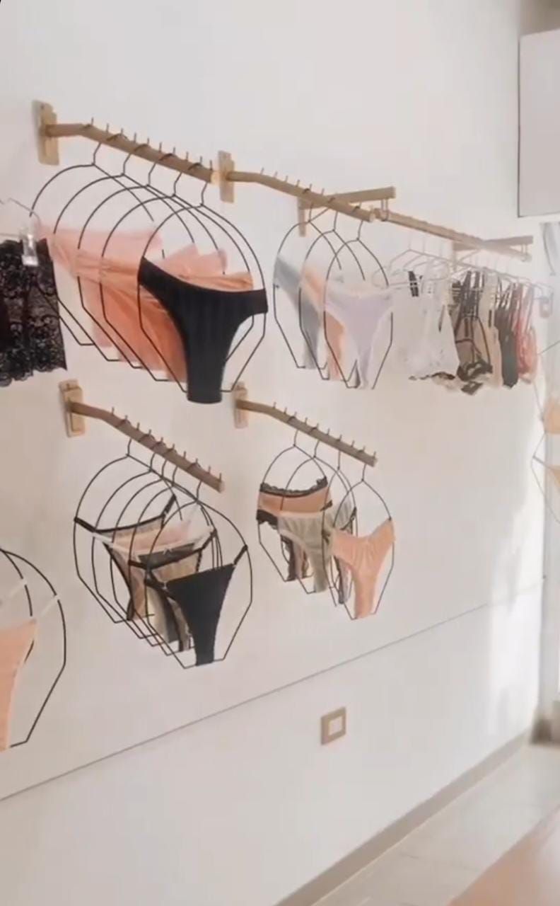 Bragas expuestas en perchas metálicas de pared. Colores surtidos: negro, piel y blanco. Entorno de venta.