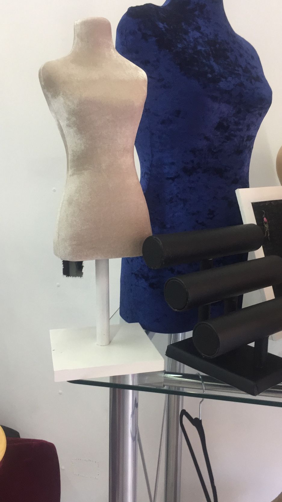 Maniquíes de tela beige y azul, expositores de joyas sobre mesa de cristal.