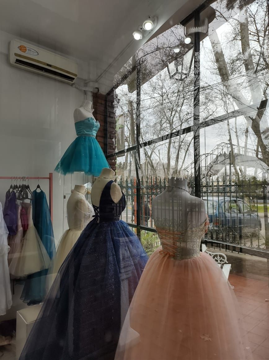 Vestidos formales en maniquíes en un escaparate, con un reflejo de la vista de la calle.