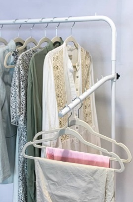 Perchero con diversas prendas, entre ellas una camisa blanca bordada y un pantalón beige.