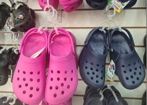 Crocs rosas y azules exhibidos en una pared junto a otros Crocs.