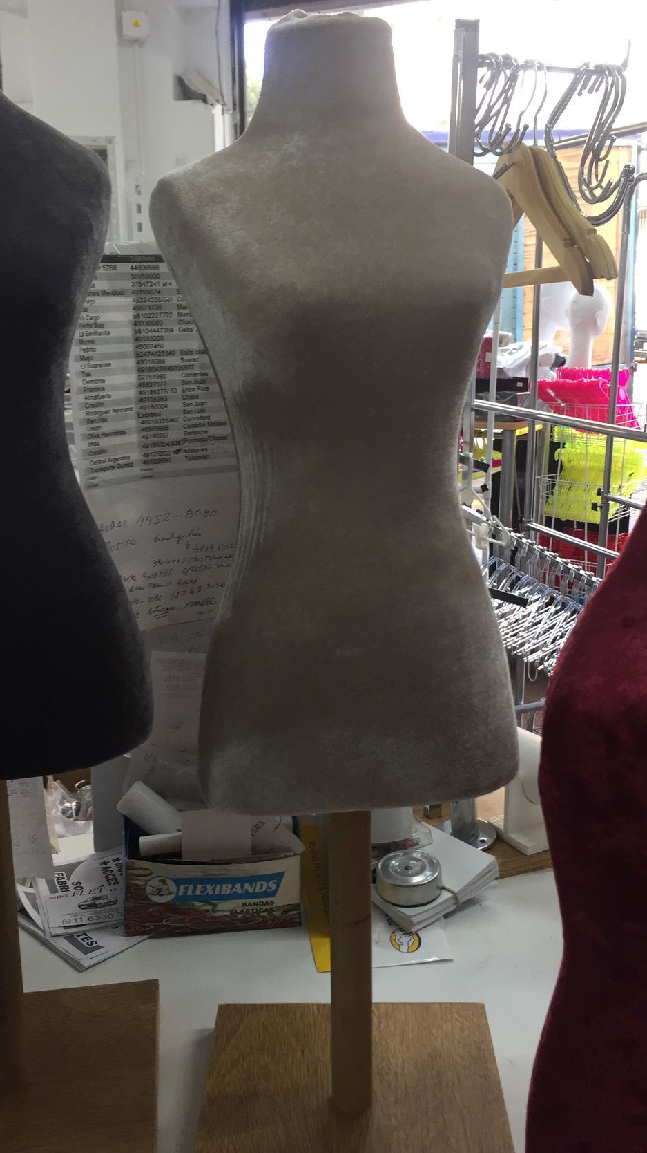 Torso de maniquí sobre soporte de madera en un taller. Tela gris, ambiente neutro.