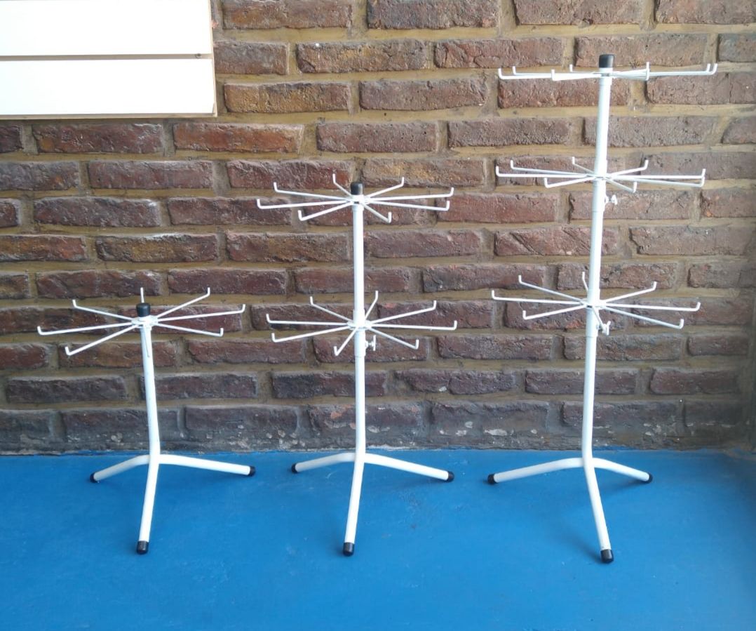 Tres expositores metálicos de color blanco con brazos giratorios, delante de una pared de ladrillos.