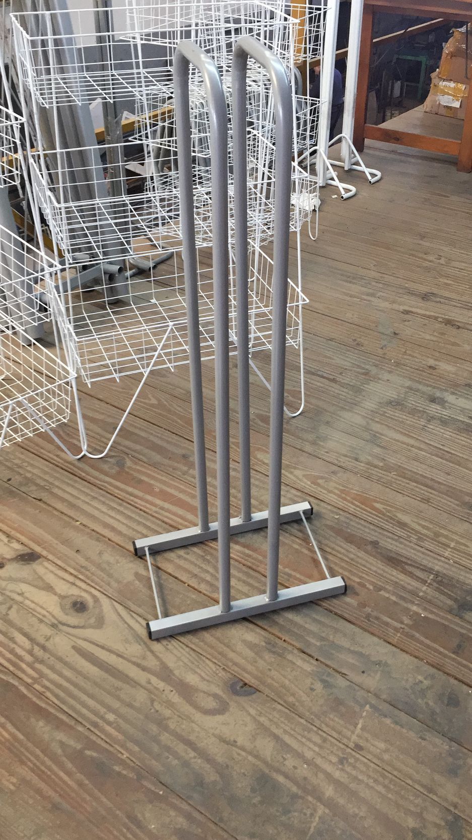 Soporte metálico con tres barras verticales sobre base rectangular, sobre suelo de madera.
