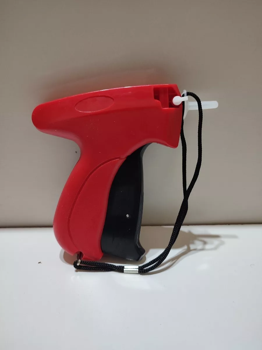 Pistola etiquetadora de prendas de color rojo y negro con una pieza de plástico blanca y un cordón negro.