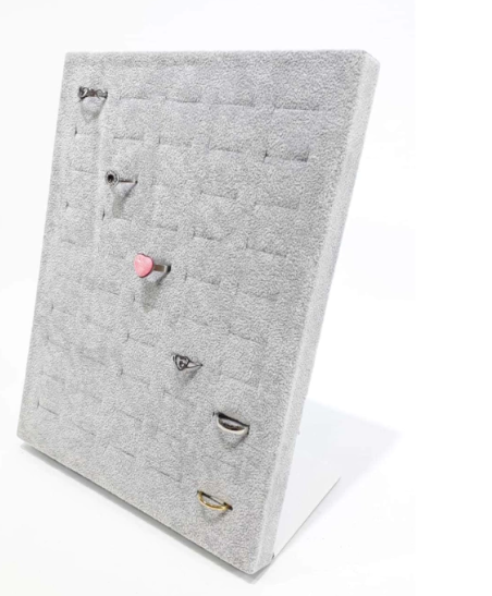 Expositor de anillos de terciopelo gris con varios anillos colocados sobre un soporte de cartón blanco.